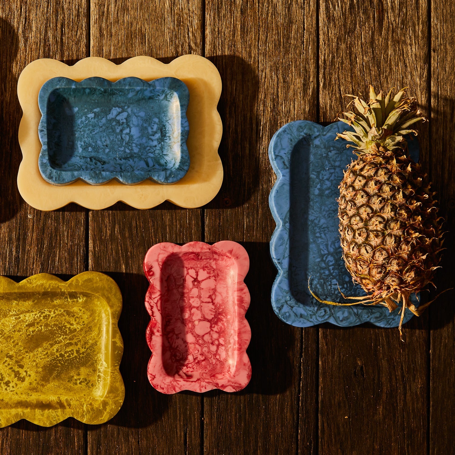 Crimson pink marbled resin scalloped tray shown in a group flat-lay with other coloured trays on wood