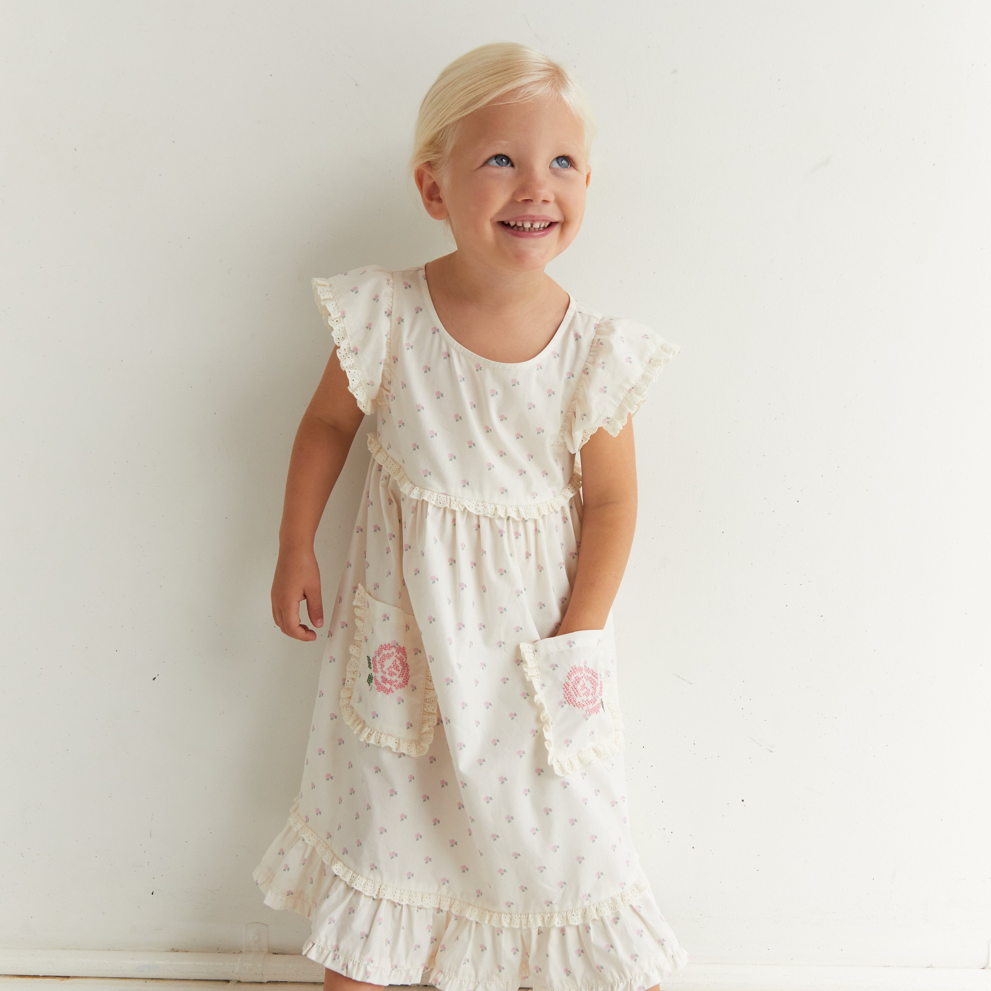 Front view of Lola Dress in white with rose pattern and embroidered pockets on child model