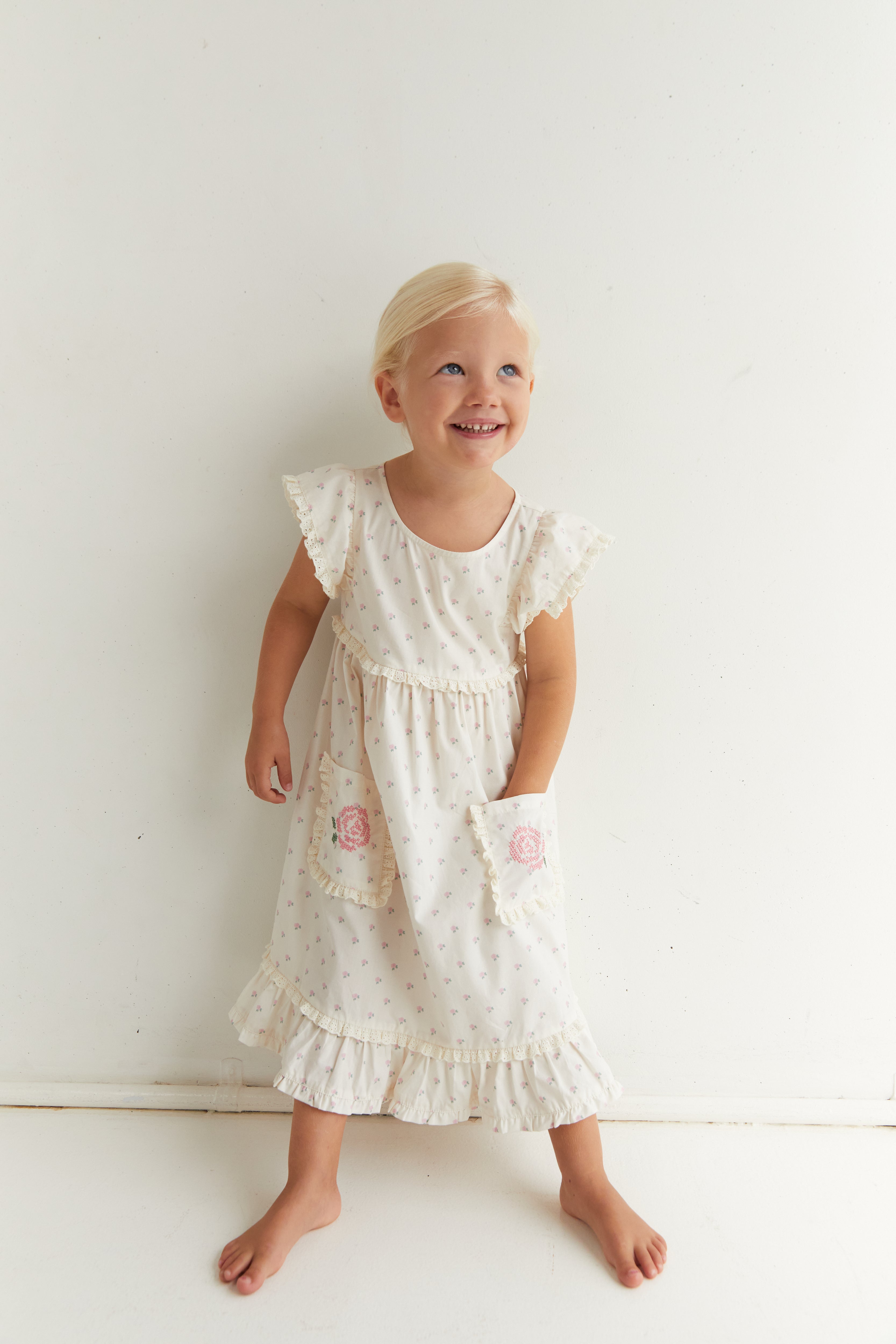 Front view of Lola Dress in white with rose pattern and embroidered pockets on child model