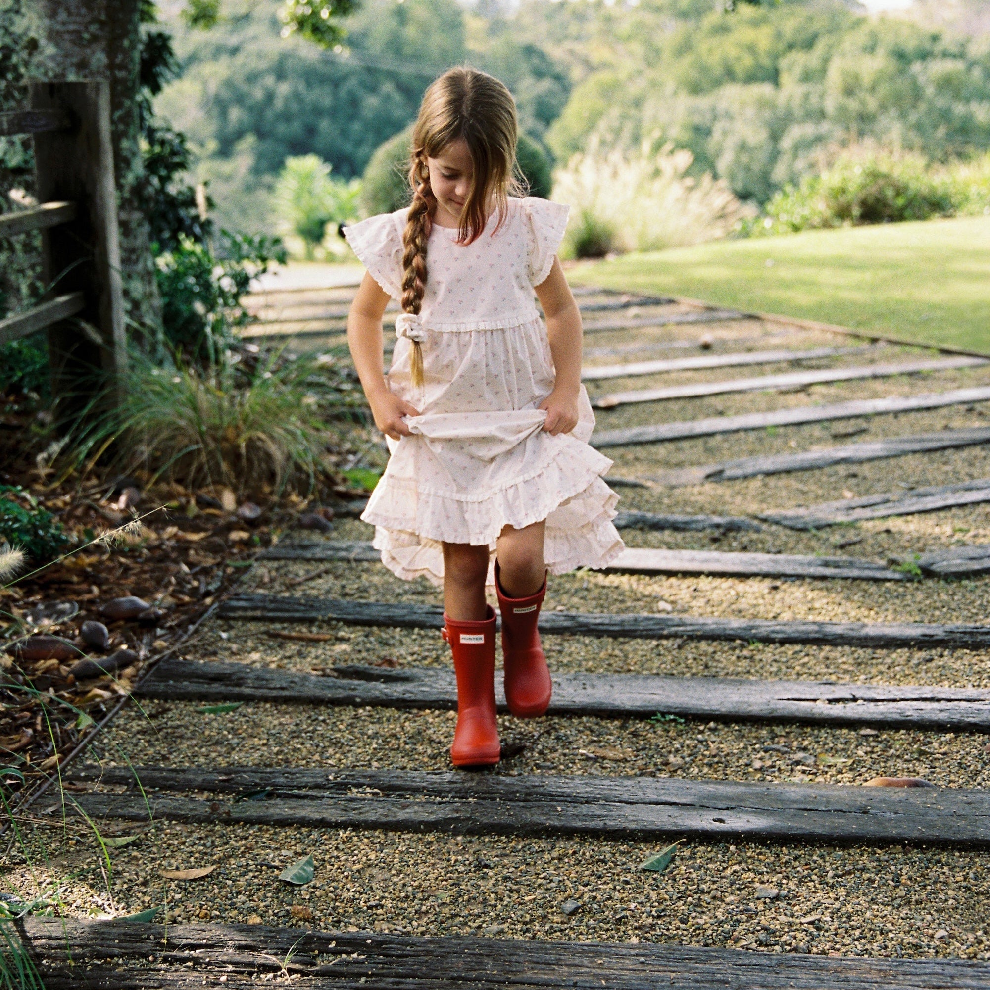 Child wearing white Lola Dress with rose pattern walking on wooden pathway outdoors
