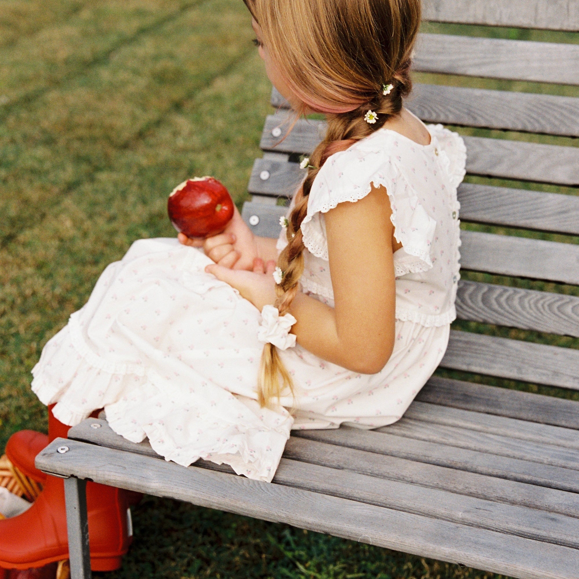 Side view of child in Lola Dress with roses print sitting on wooden bench