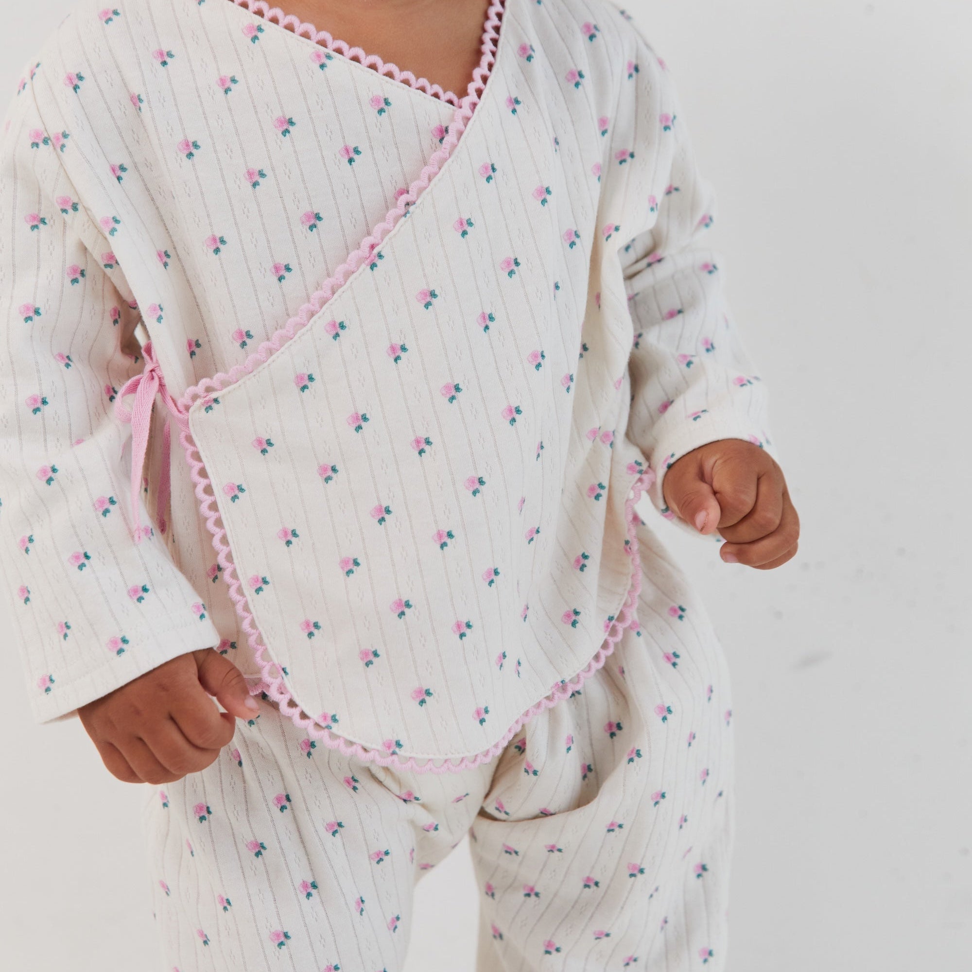 Close-up front view of child in Lolly Set wrap top with roses print and pink binding