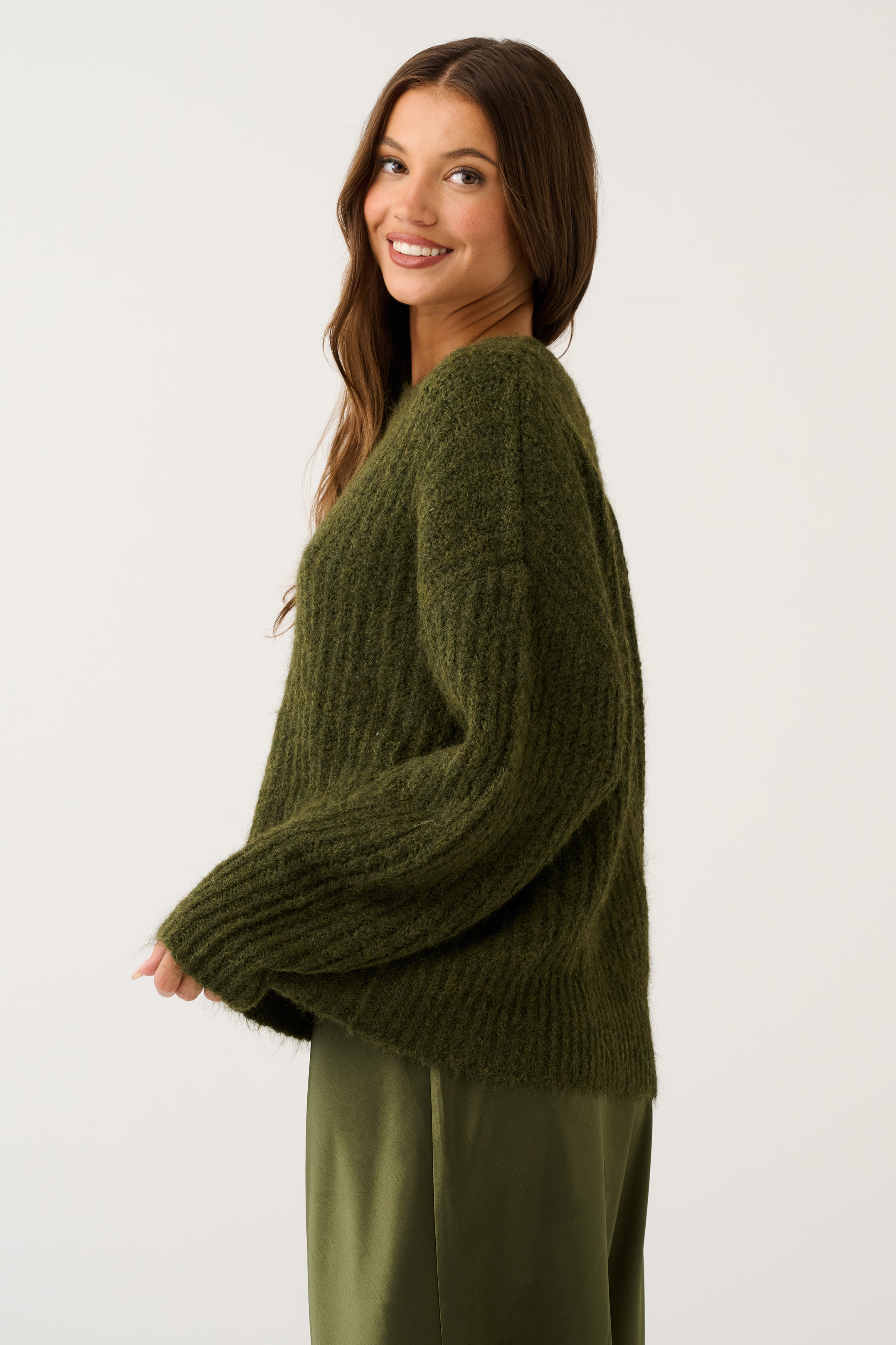 Side view of an olive green oversized chunky ribbed knit sweater showing volume and long wide sleeves