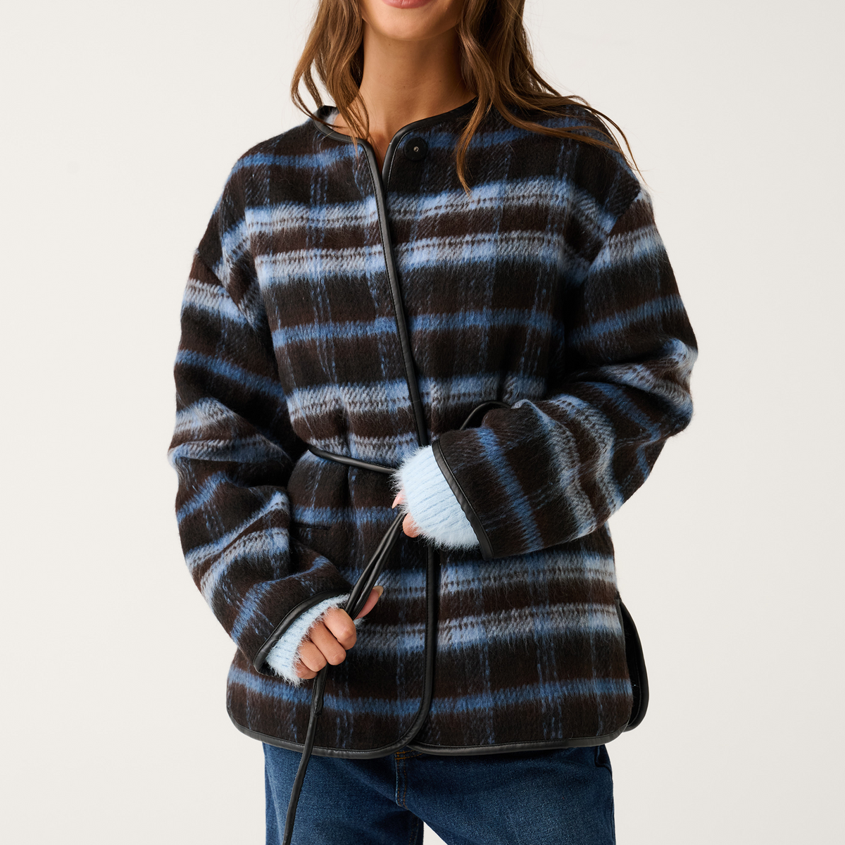 Front view of a blue and brown check oversized jacket with black leather trim, snap collar, and tie belt