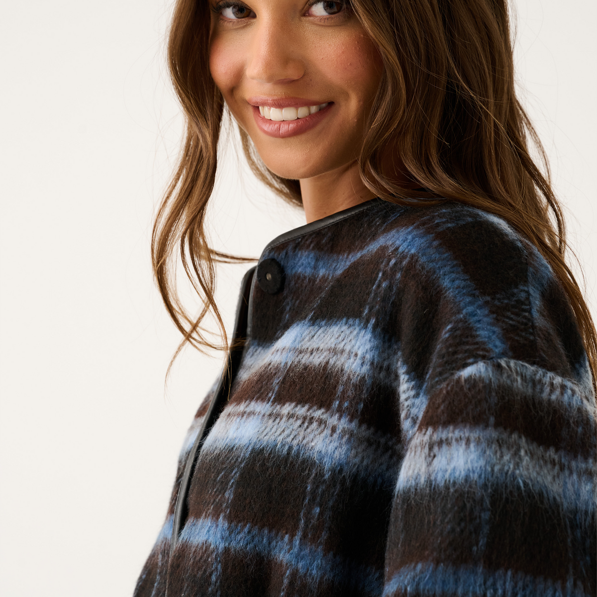 Close-up side view of a blue and brown check jacket showing the black leather trim neckline and snap button