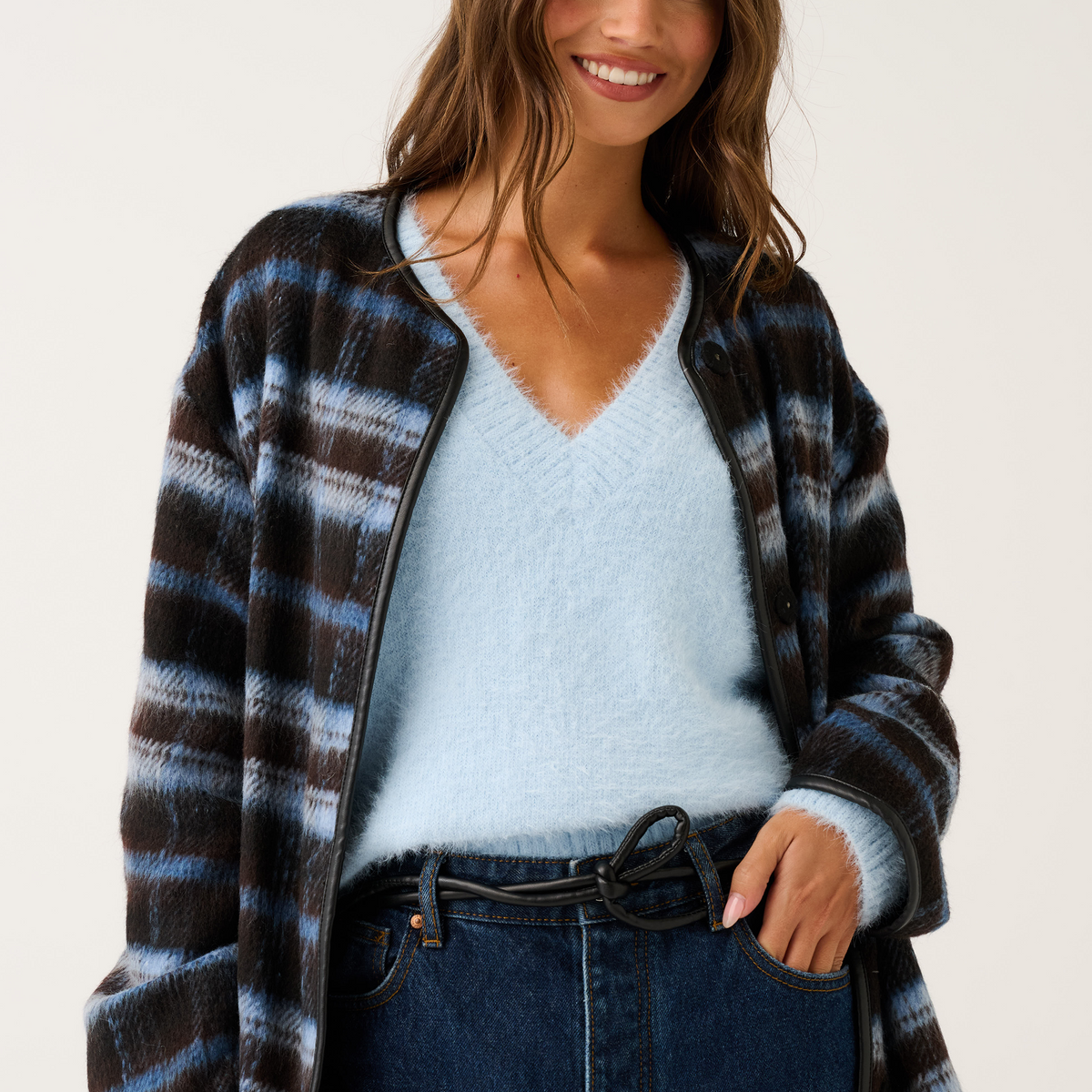 Open-front blue and brown check jacket with black leather trim worn over a pale blue knit sweater and jeans