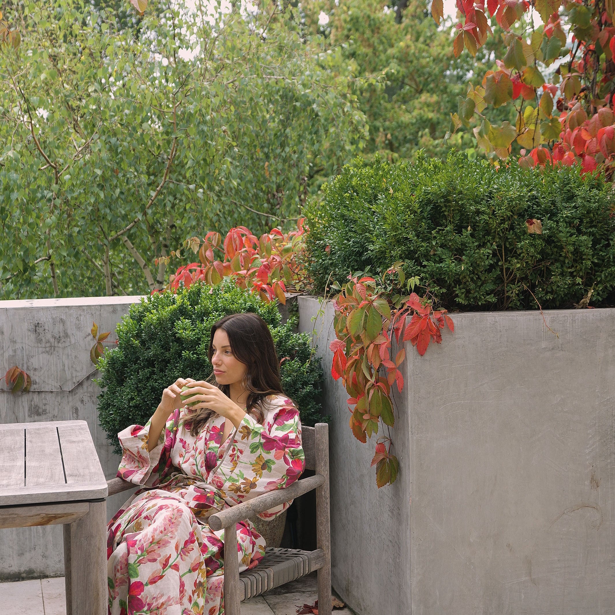Side view of woman in Lupin Multi Linen Robe with botanical print sitting outdoors on wooden chair