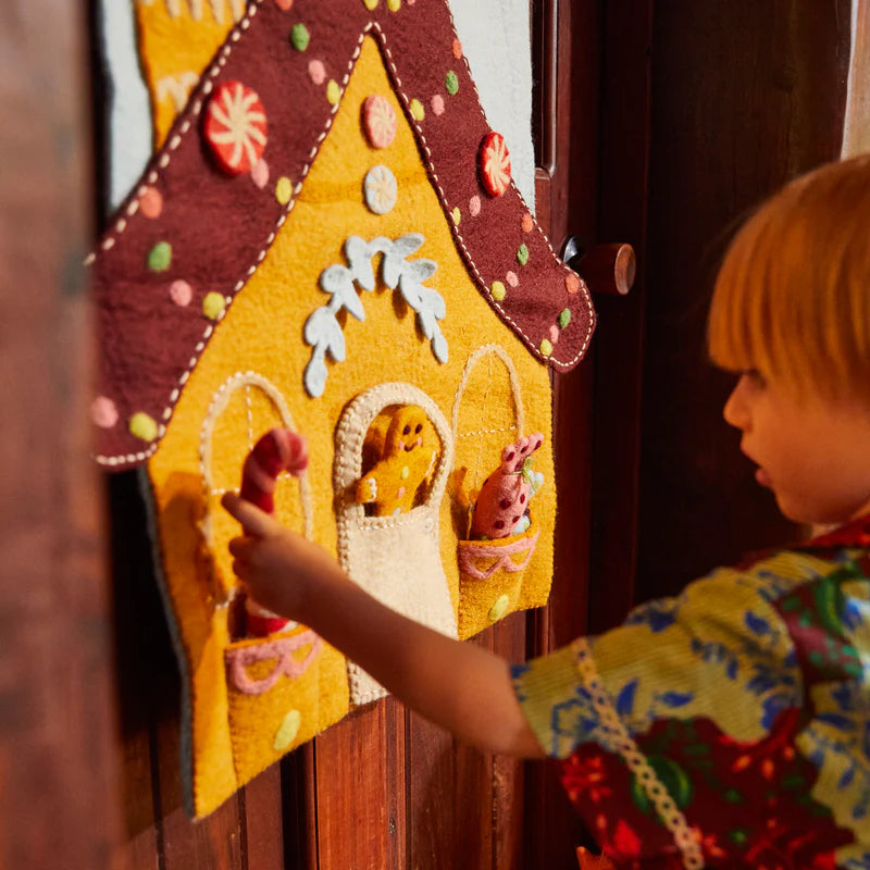 Child putting felt toys into Lyon Gingerbread House Wall Hanging by Sage & Clare