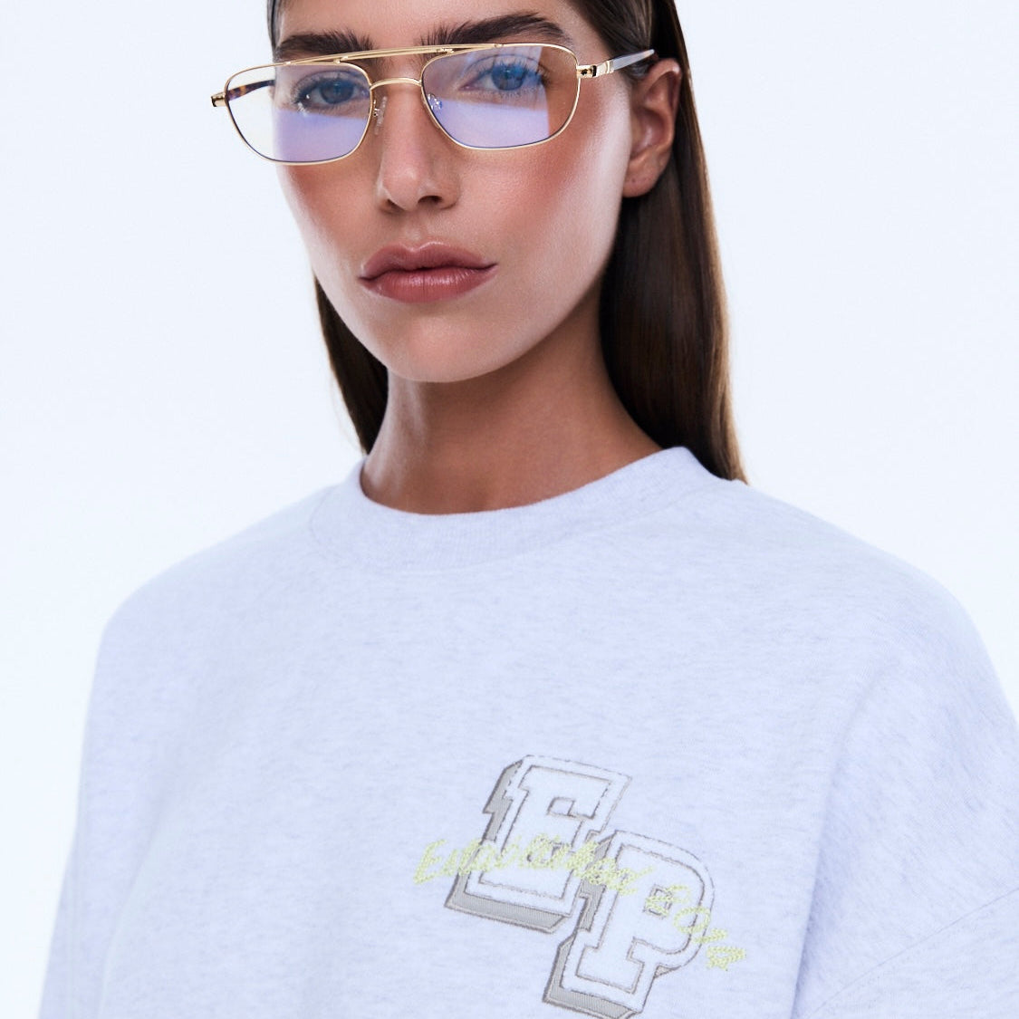 Close-up view of white oversized sweater showing embroidered chest logo detail