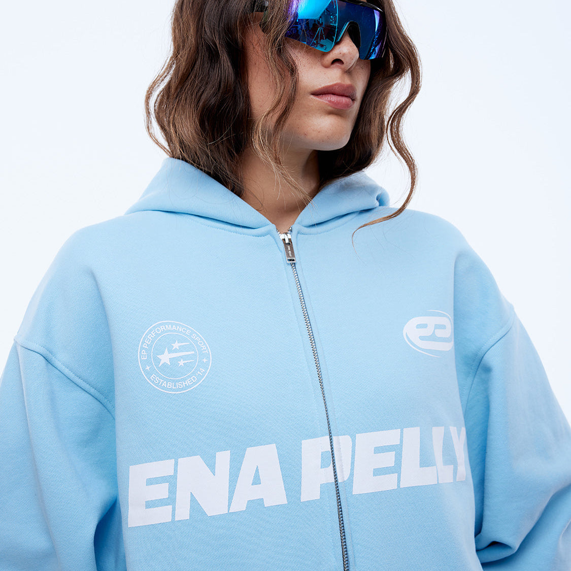 Close-up front view of cloud blue zip-up hoodie showing multi logo design and hood detail