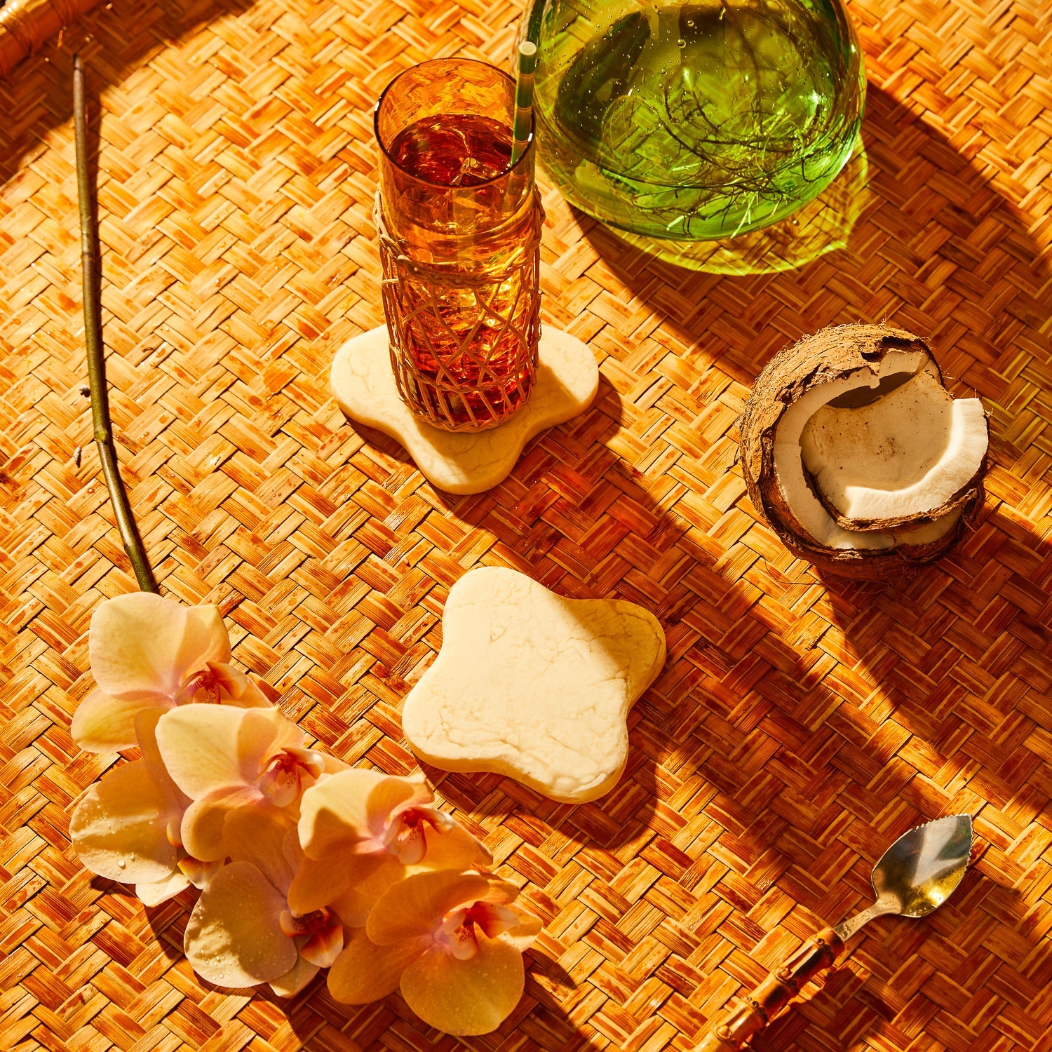 Pearl cream marbled resin coasters on a rattan tray styled with orchids and a drink glass, overhead view