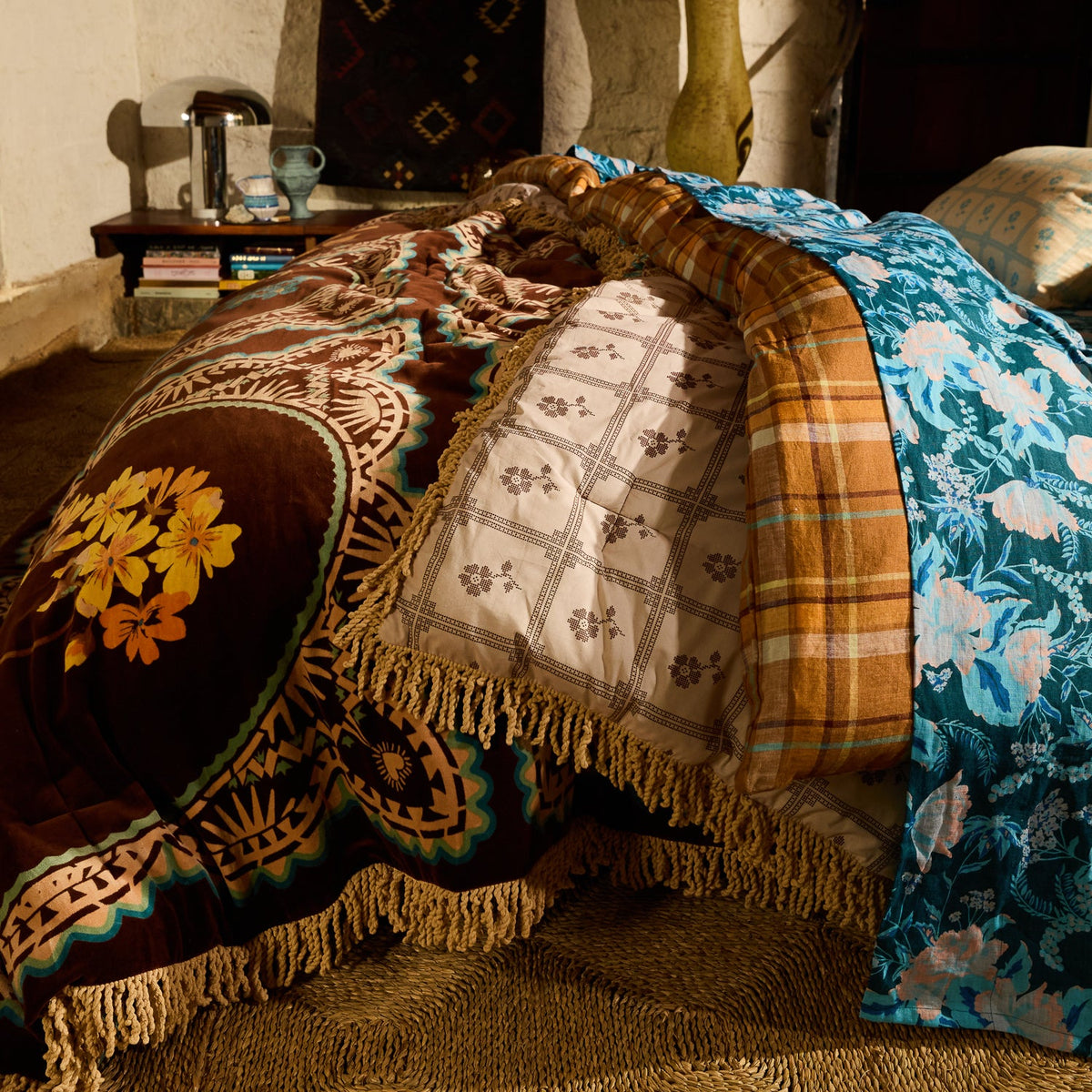 Close-up of brown velvet bedcover with yellow floral medallion print and gold fringe trim layered on a styled bed