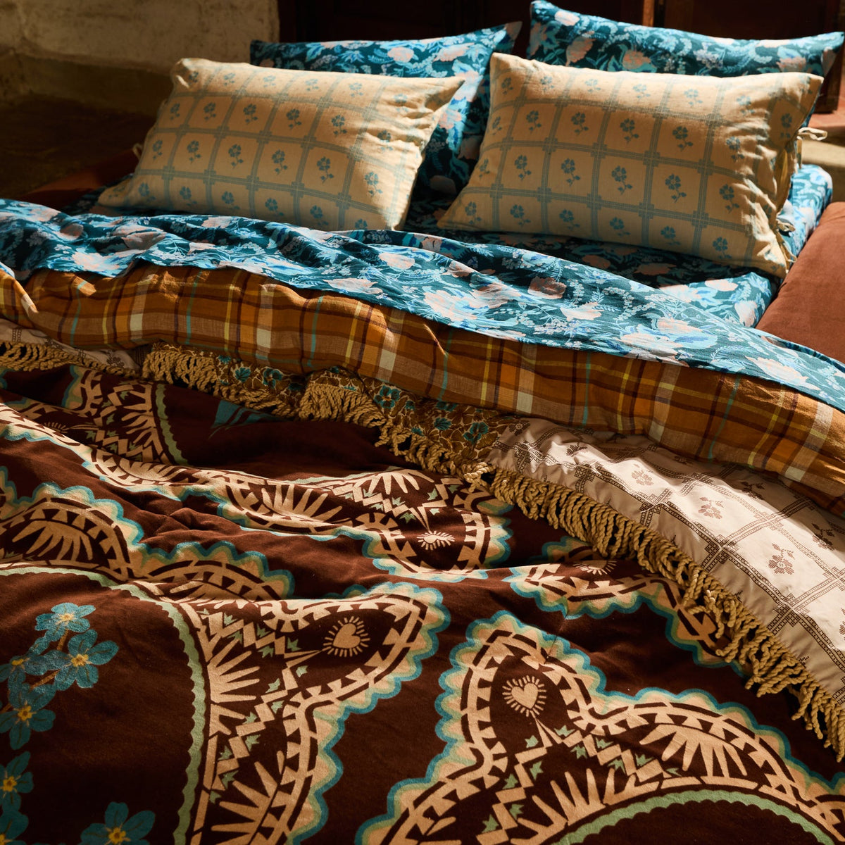Detail shot of brown velvet bedcover featuring teal and tan paisley medallion pattern with gold fringe edge on a bed