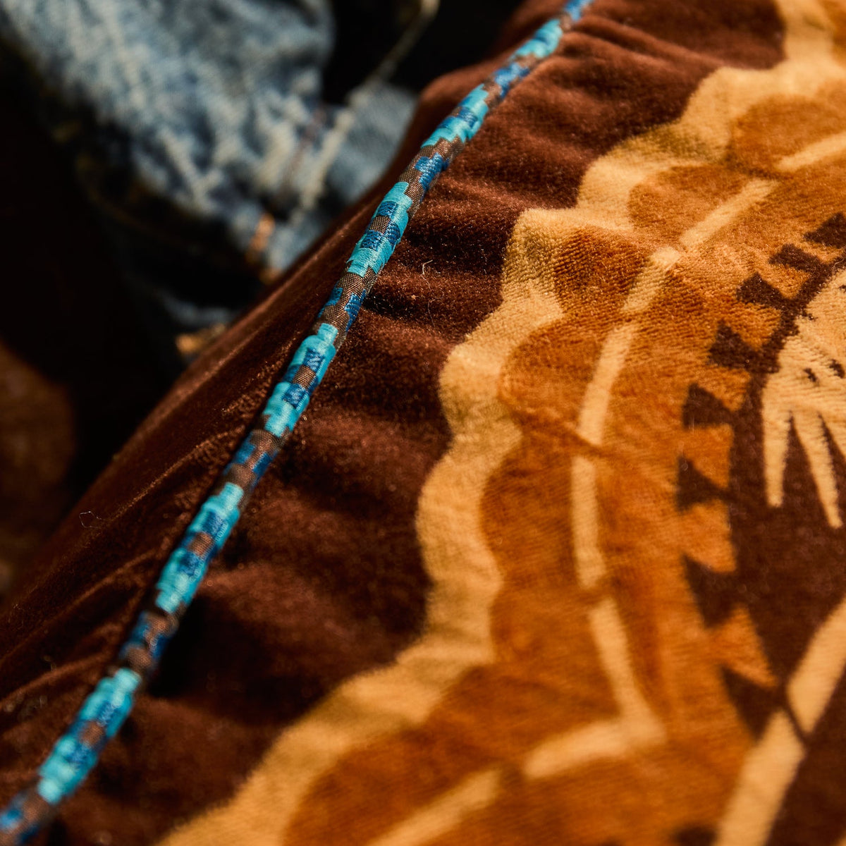 Close-up of teal patterned piping trim on the edge of a brown printed velvet cushion cover