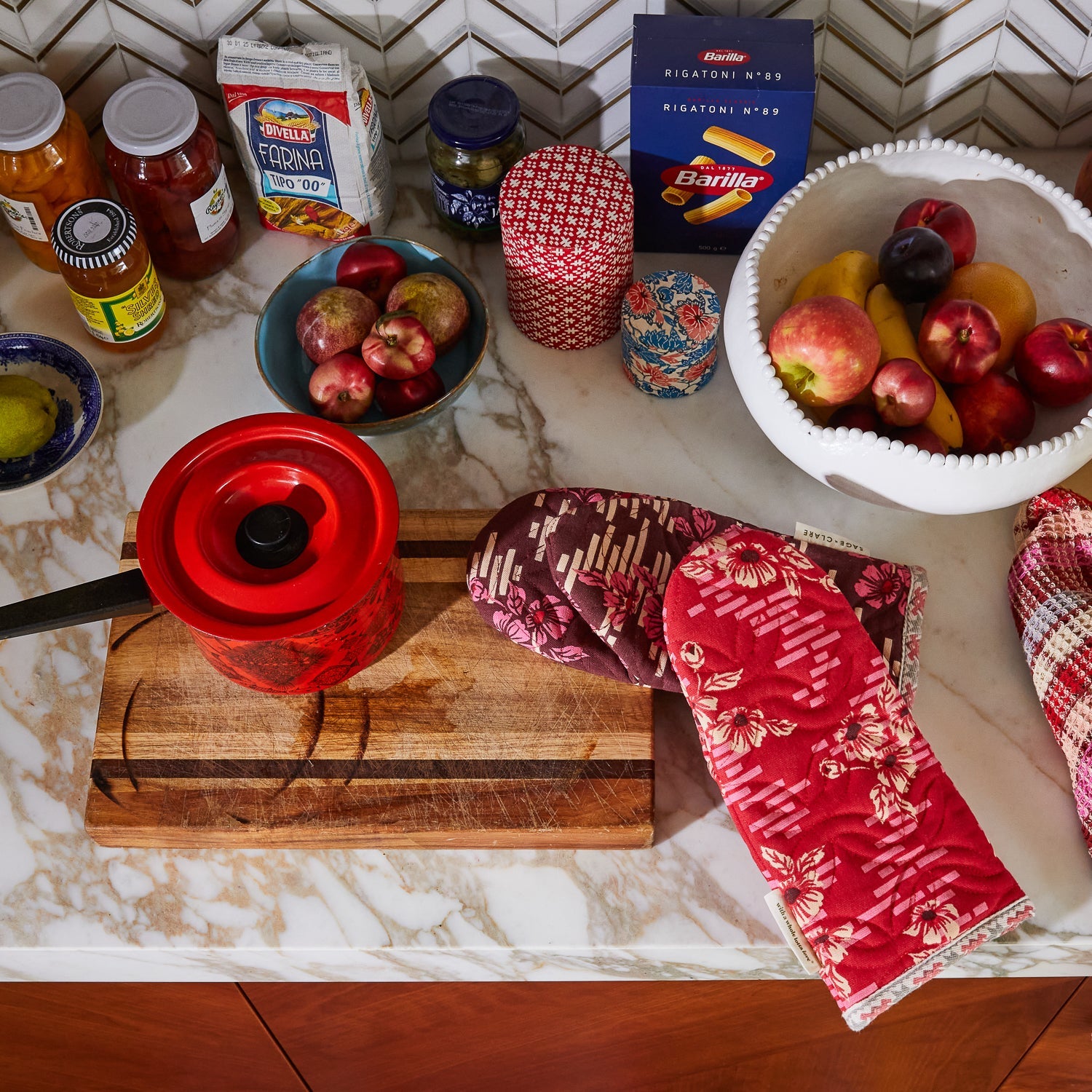 Sage and Clare Marta Oven Mitts displayed on marble kitchen counter with cooking accessories and pantry items