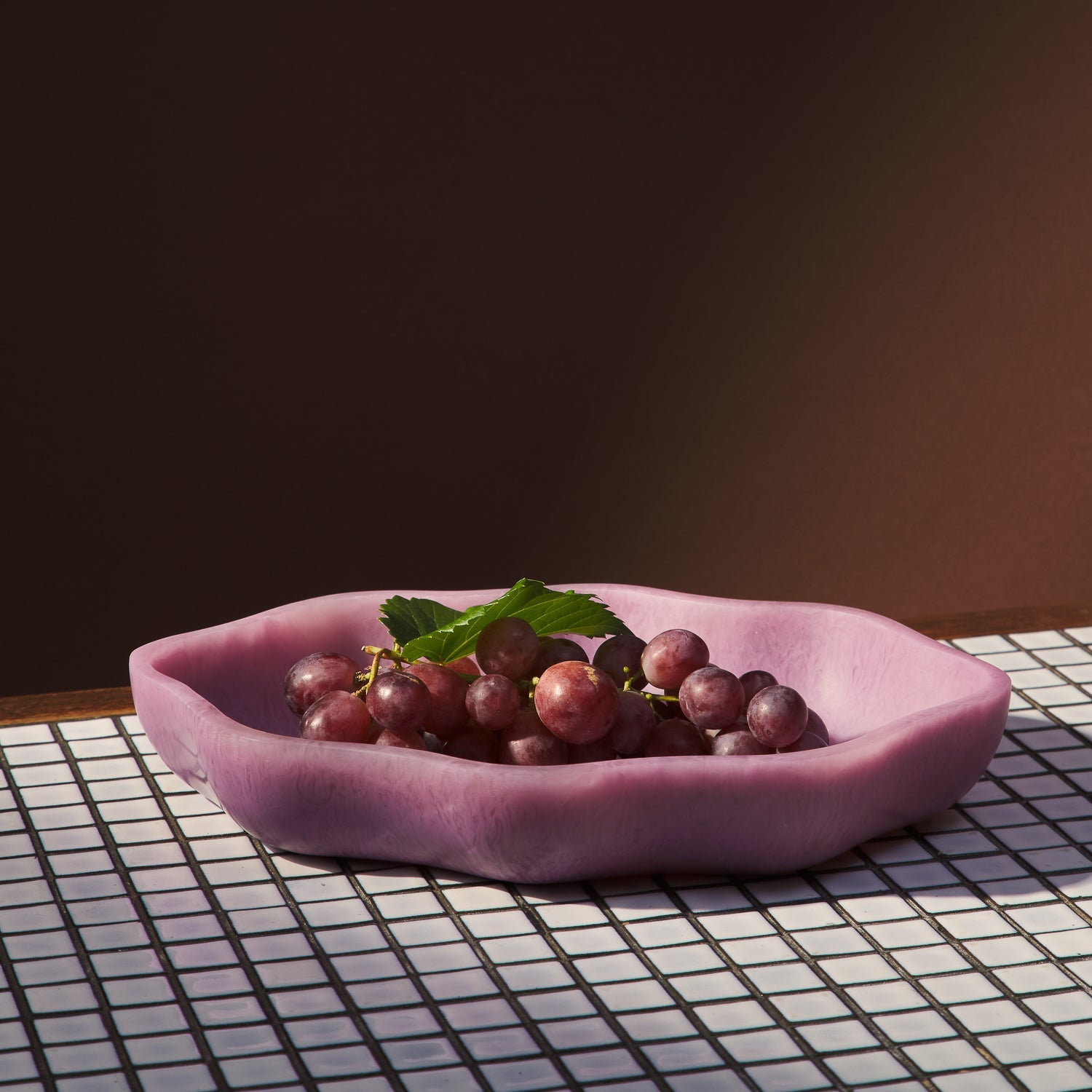 Pink serving dish filled with red grapes on checkered placemat showing functional use