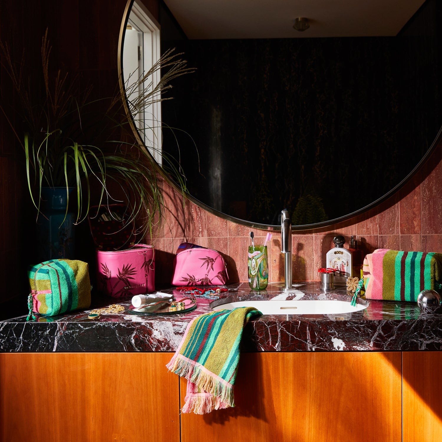 Bathroom vanity styling with multiple Nicolette Terry Pouches and matching striped towel in modern marble setting
