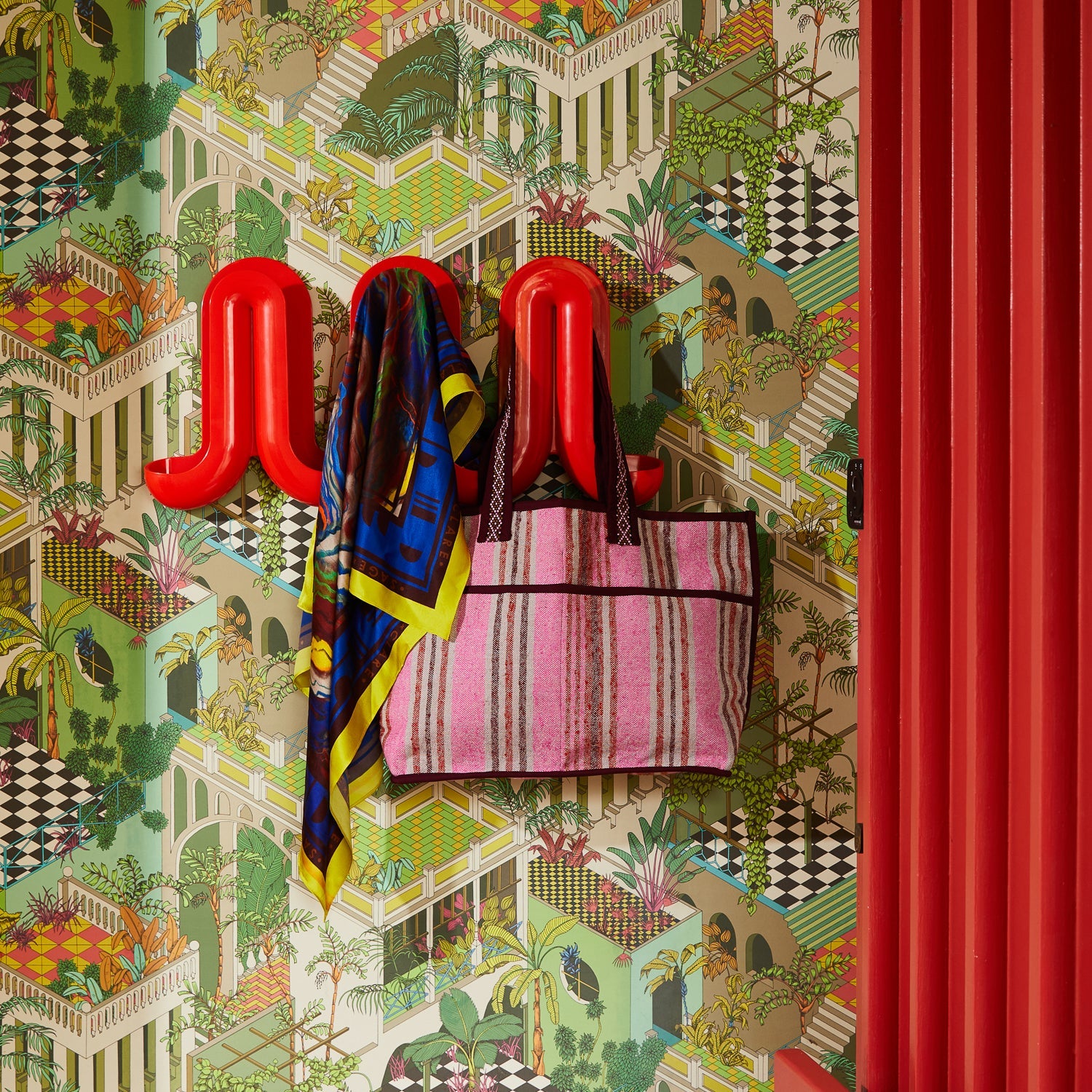 Nicolette Woven Tote Bag in Pansy hanging on red hook against tropical wallpaper background