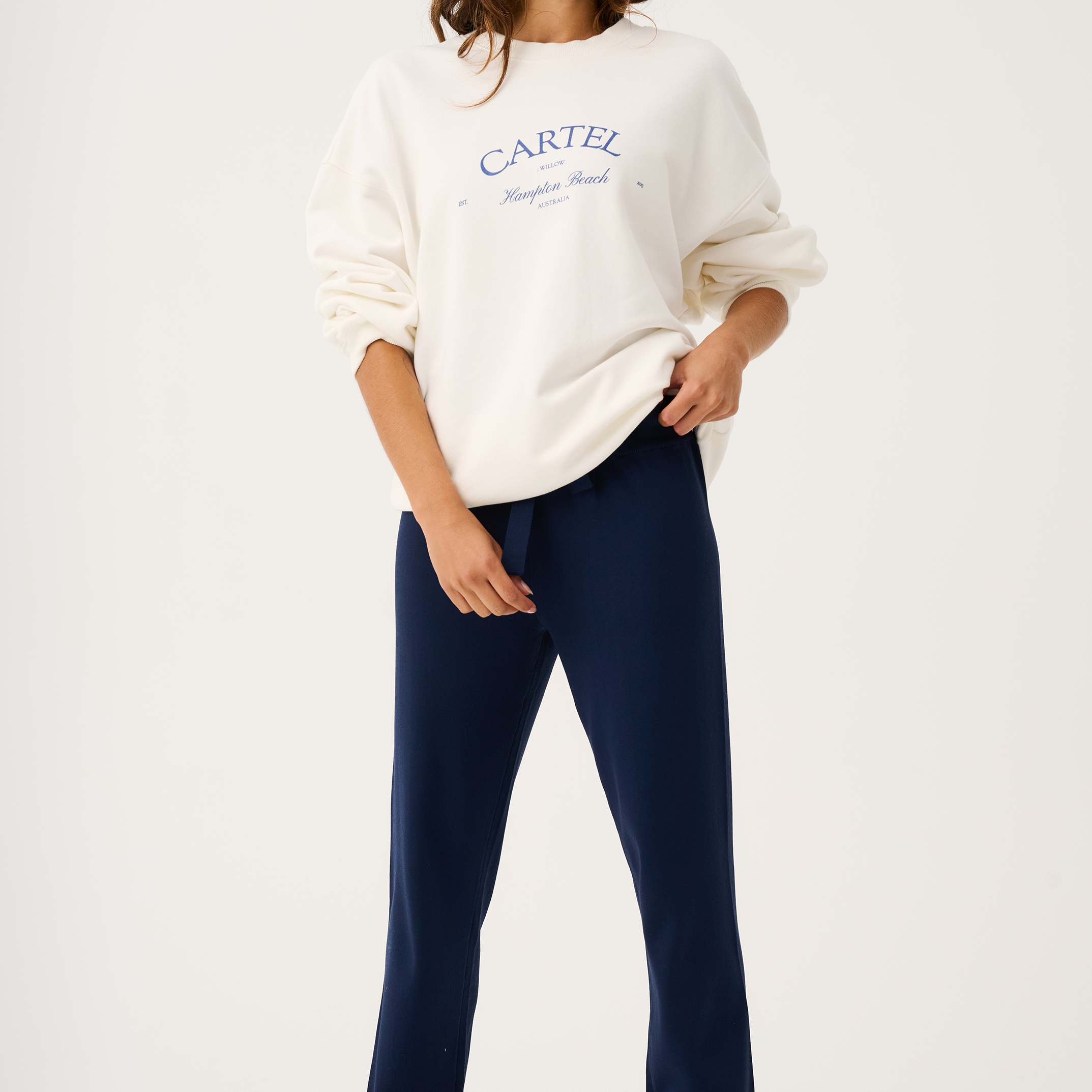 Full body view of white Nina Sweater with blue text paired with navy pants