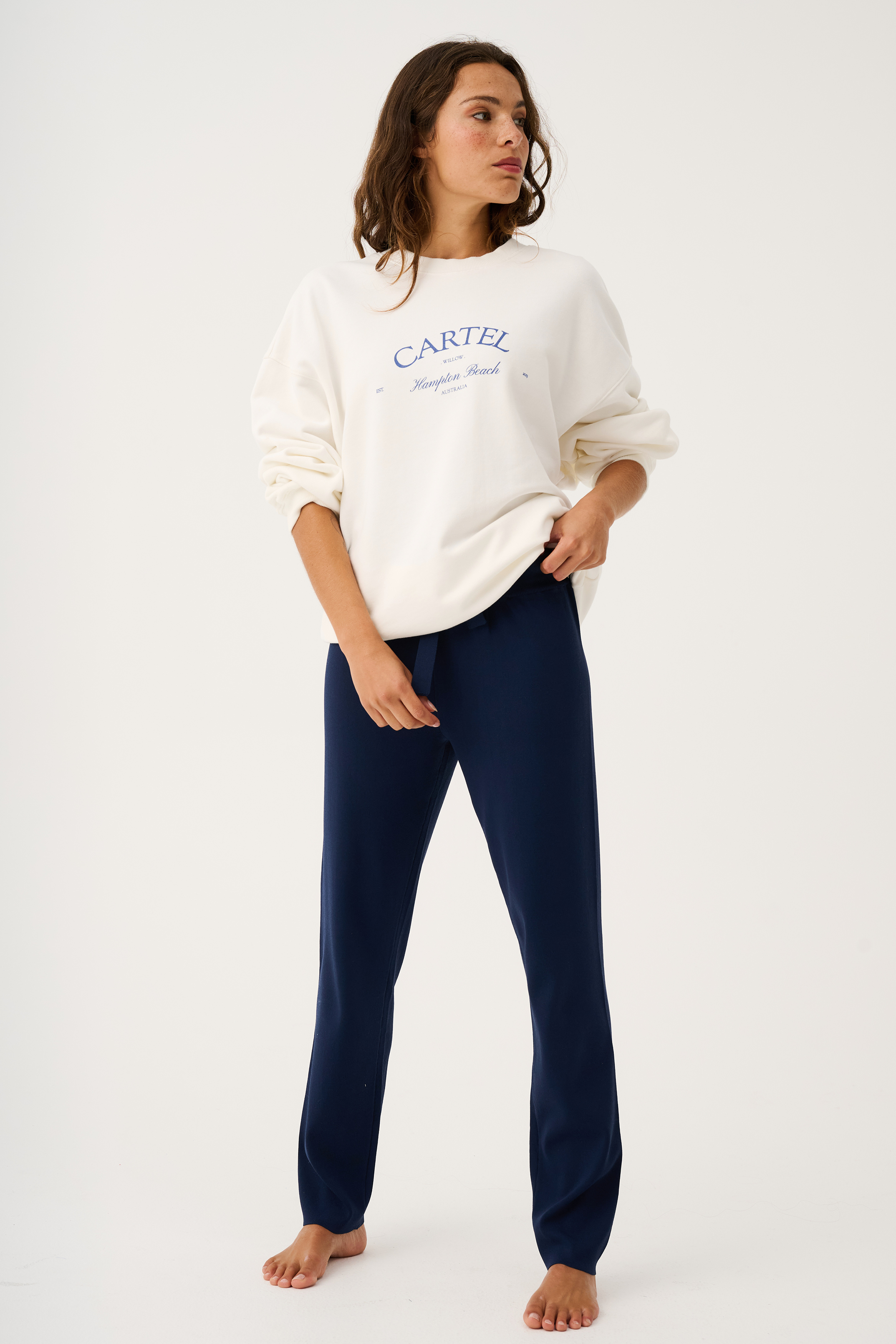 Full body view of white Nina Sweater with blue text paired with navy pants