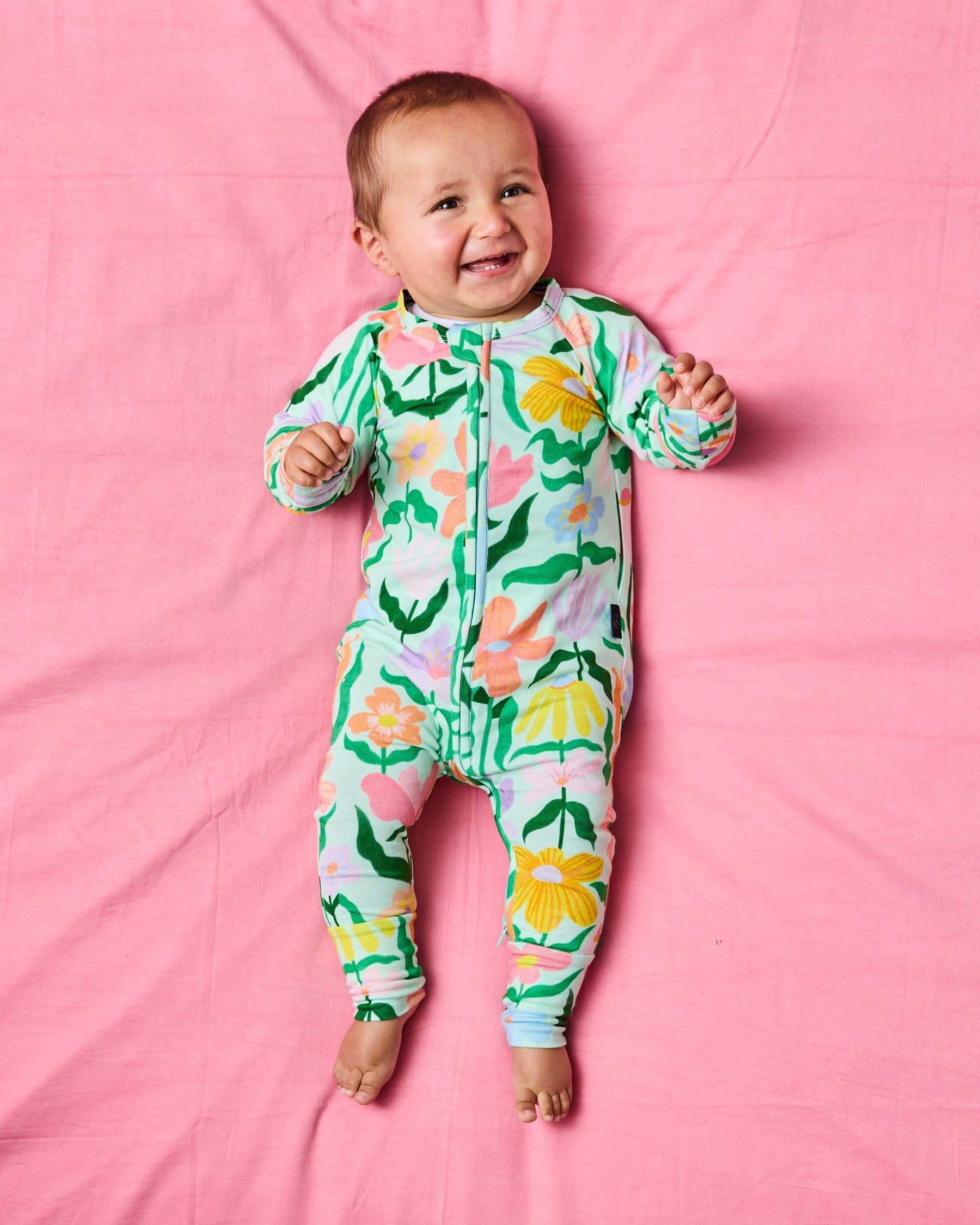 Full body view of Popping Flowers Green Organic Long Sleeve Zip Romper by Kip & Co on pink background