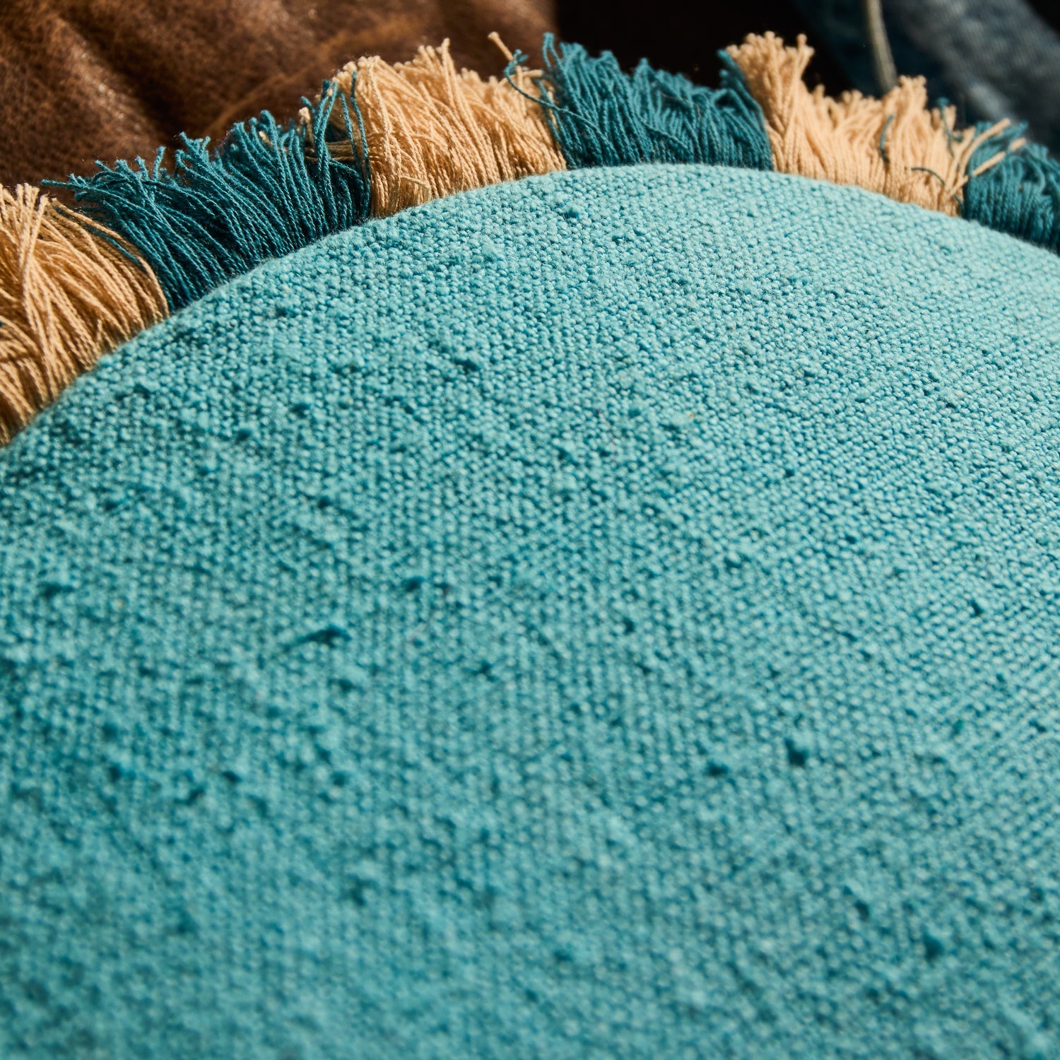 Close-up of the textured woven turquoise fabric and fringe edge on a round cushion