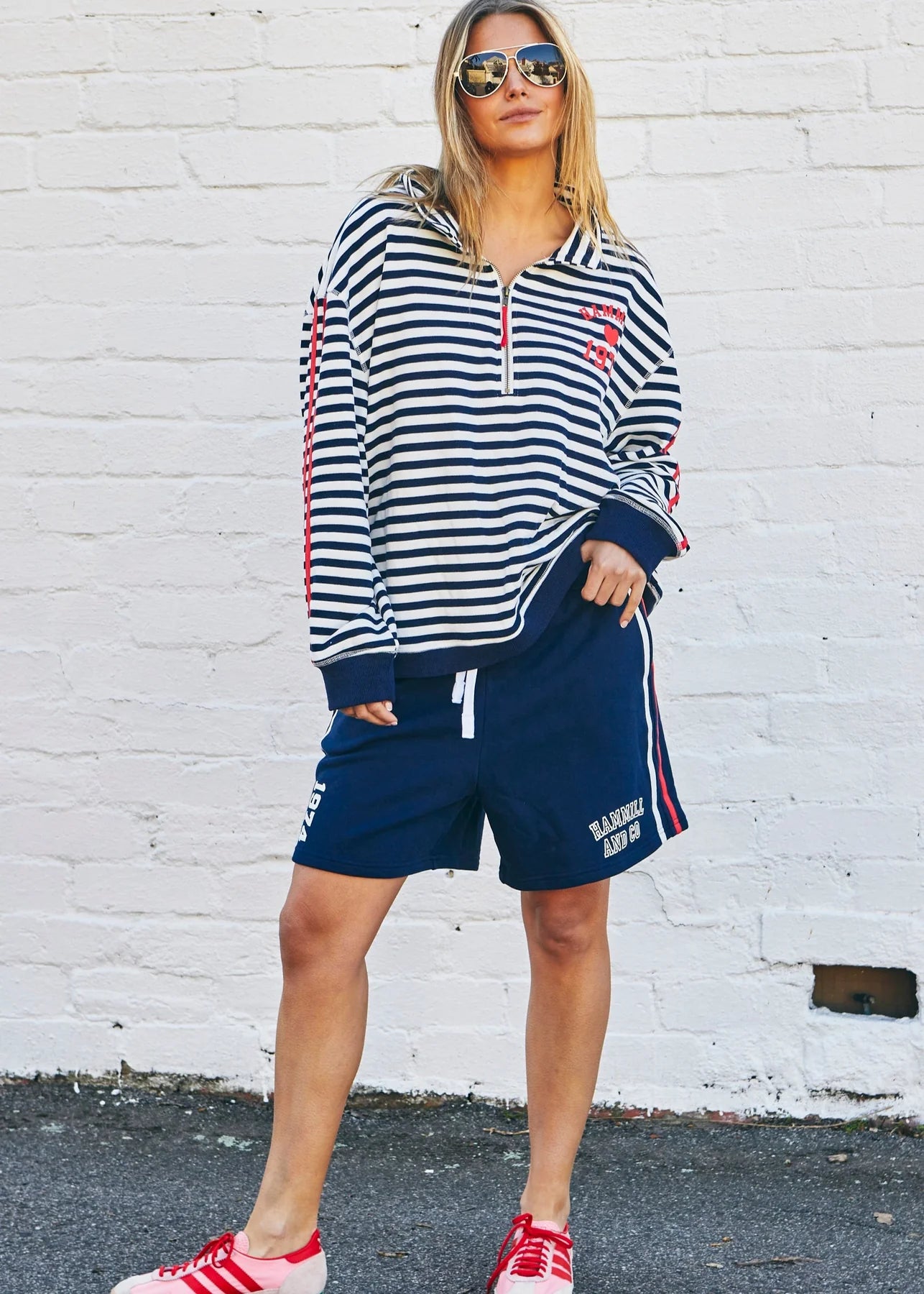 Woman wearing a striped hoodie and shorts with red accents against a white brick wall.
