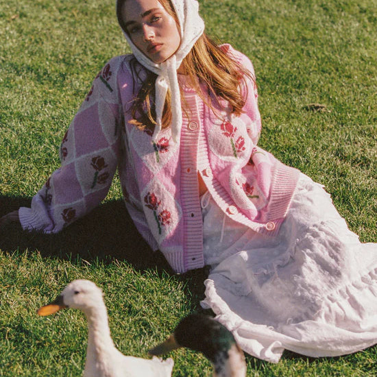 female model sitting down wearing the Rosie Cardigan by JUNI with ducks around her