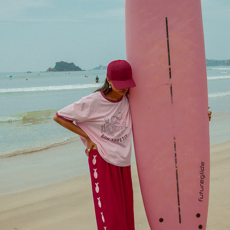 model wearing Sardine Pants by Palm Collective next to pink surfboard