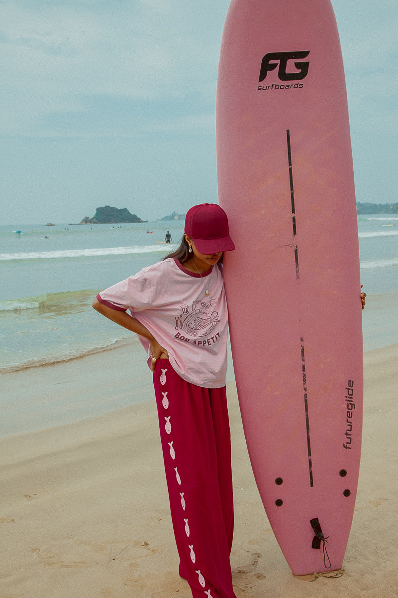 model wearing Sardine Pants by Palm Collective next to pink surfboard