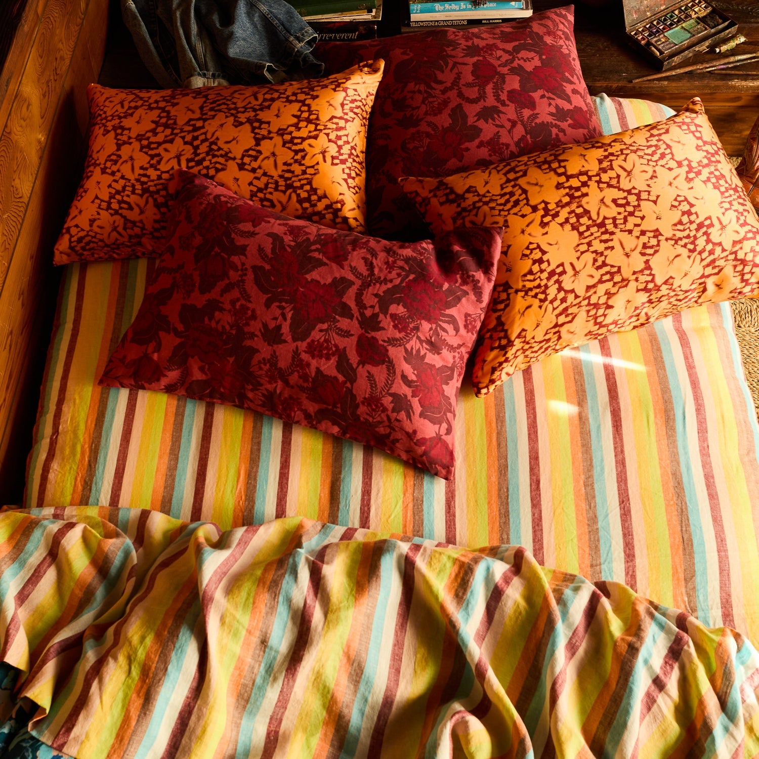 Red and orange floral linen pillowcases styled on a bed with a multicolour striped sheet, overhead view