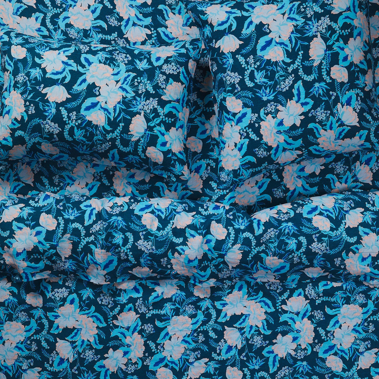 Close-up overhead shot of teal and blush floral linen sheets and pillowcases on a bed