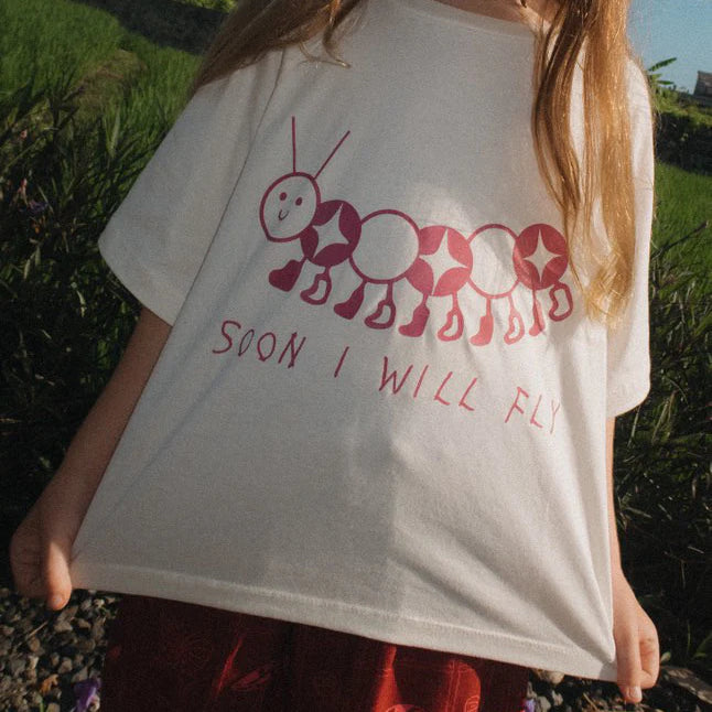child wearing Soon I will Fly Tee by Sauce Mini with burgundy caterpillar graphic on the front