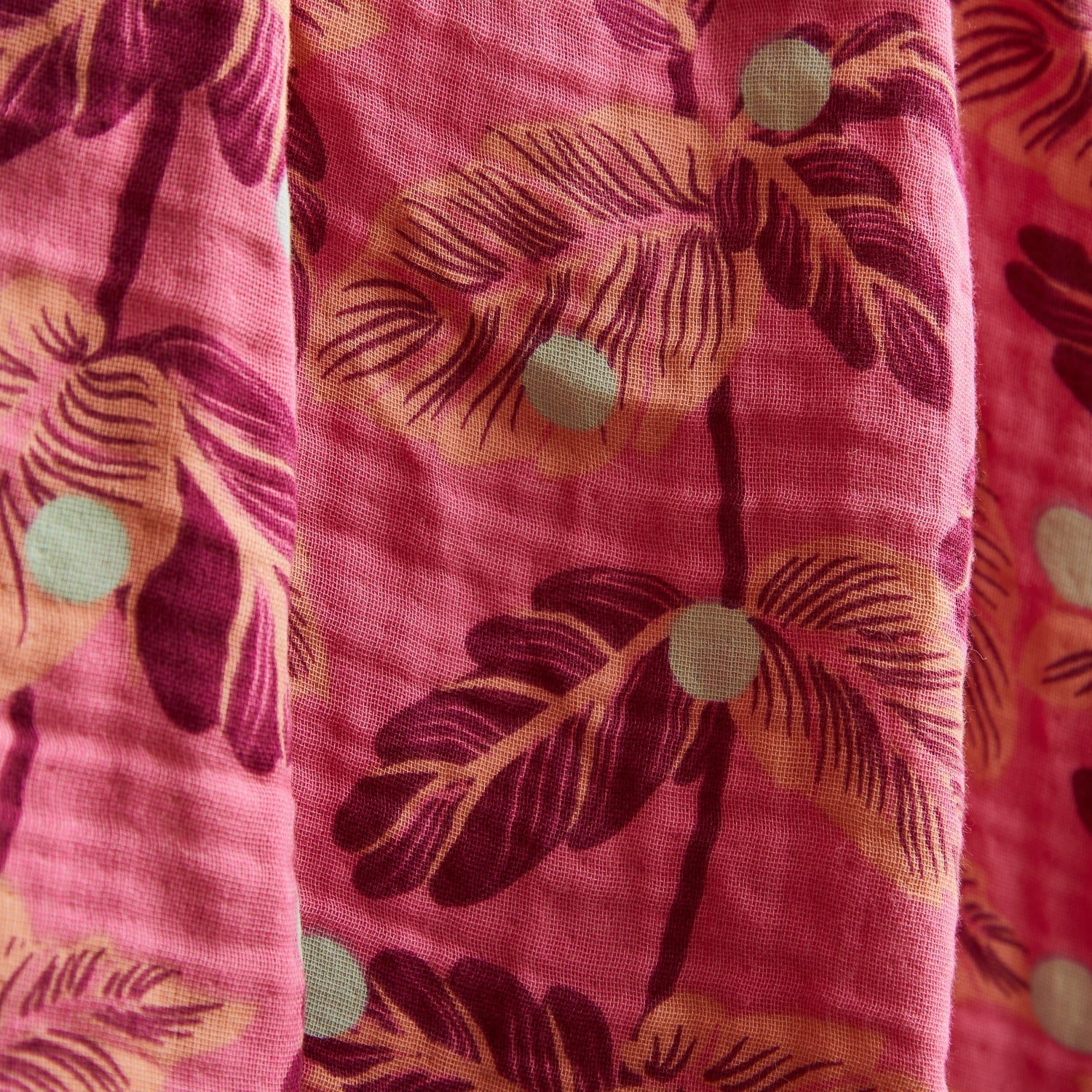Close-up view of pink baby wrap fabric showing tropical leaf print and woven cotton texture