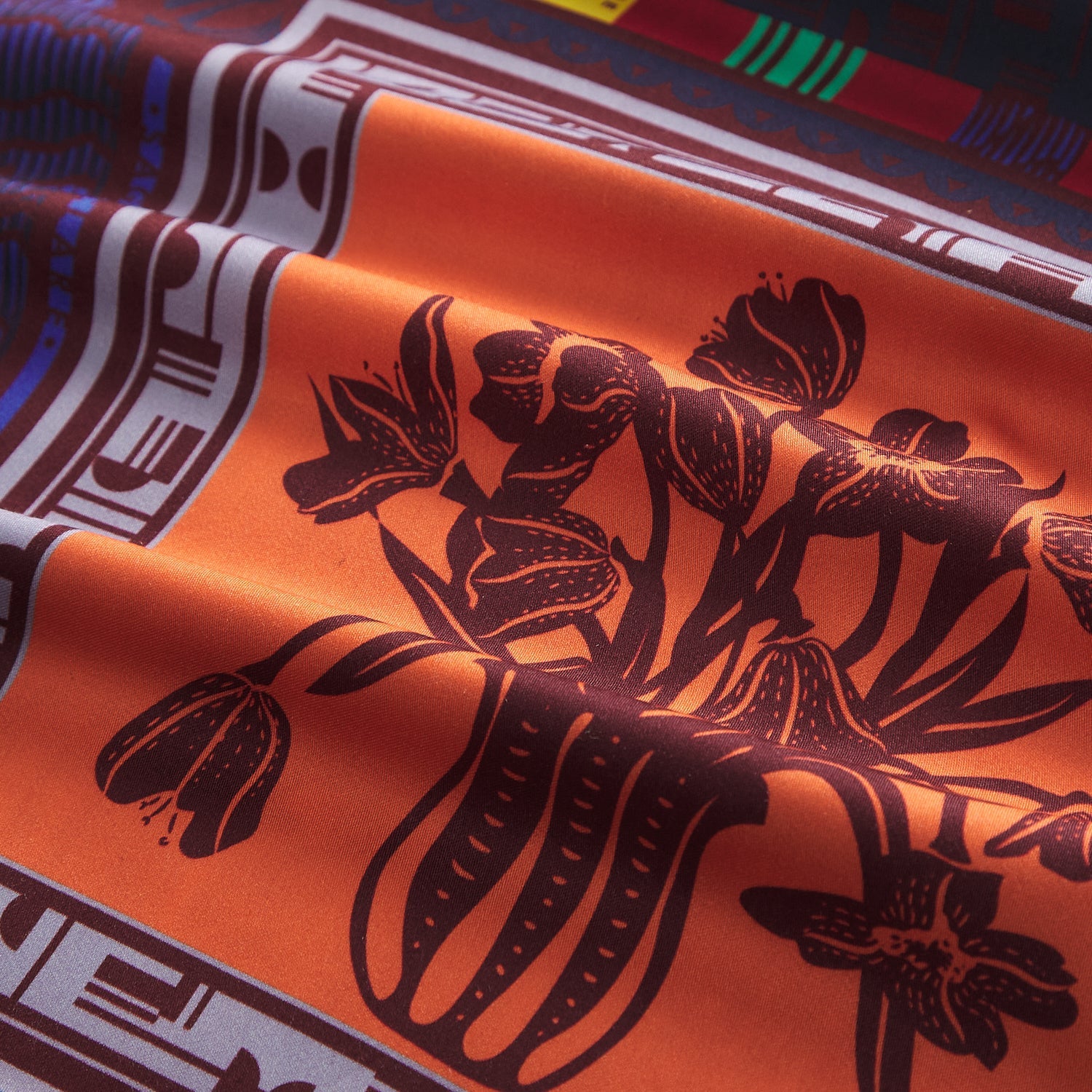 Close-up fabric detail of the maxi dress showing an orange panel with dark botanical floral print and geometric border