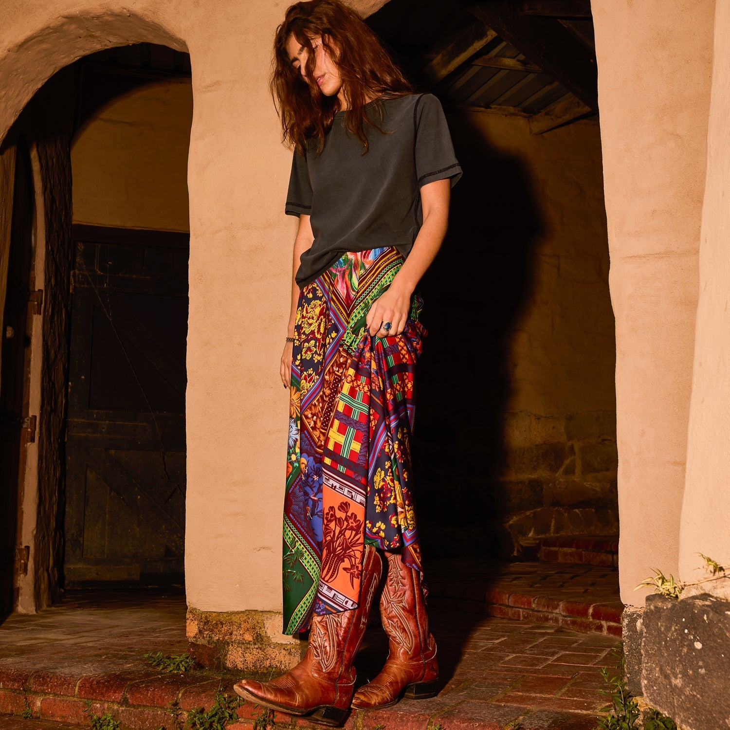 Front view of a multicolour patchwork-print satin maxi slip skirt styled with a grey tee and brown cowboy boots