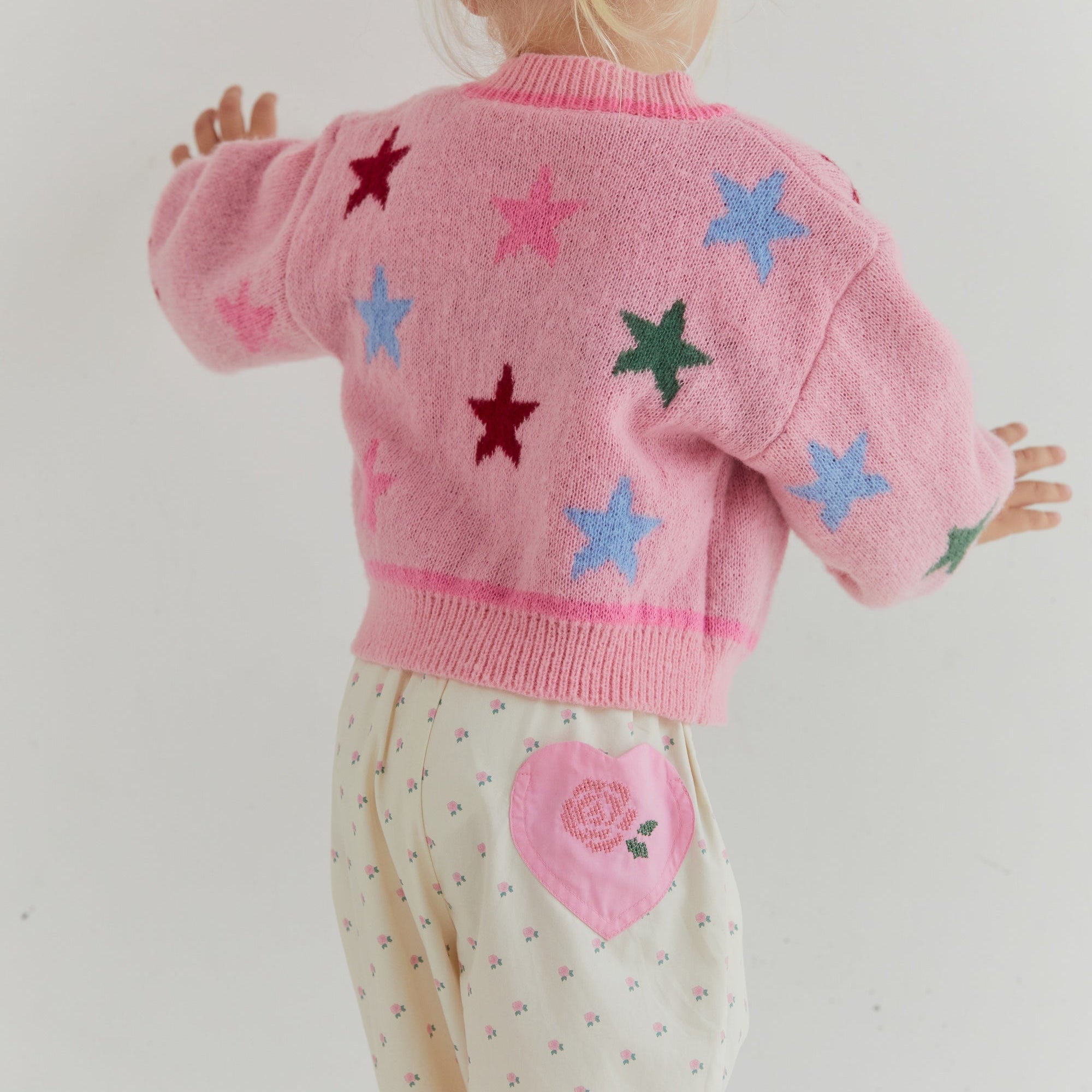 Back view showing star pattern distribution on pink knit cardigan with ribbed collar