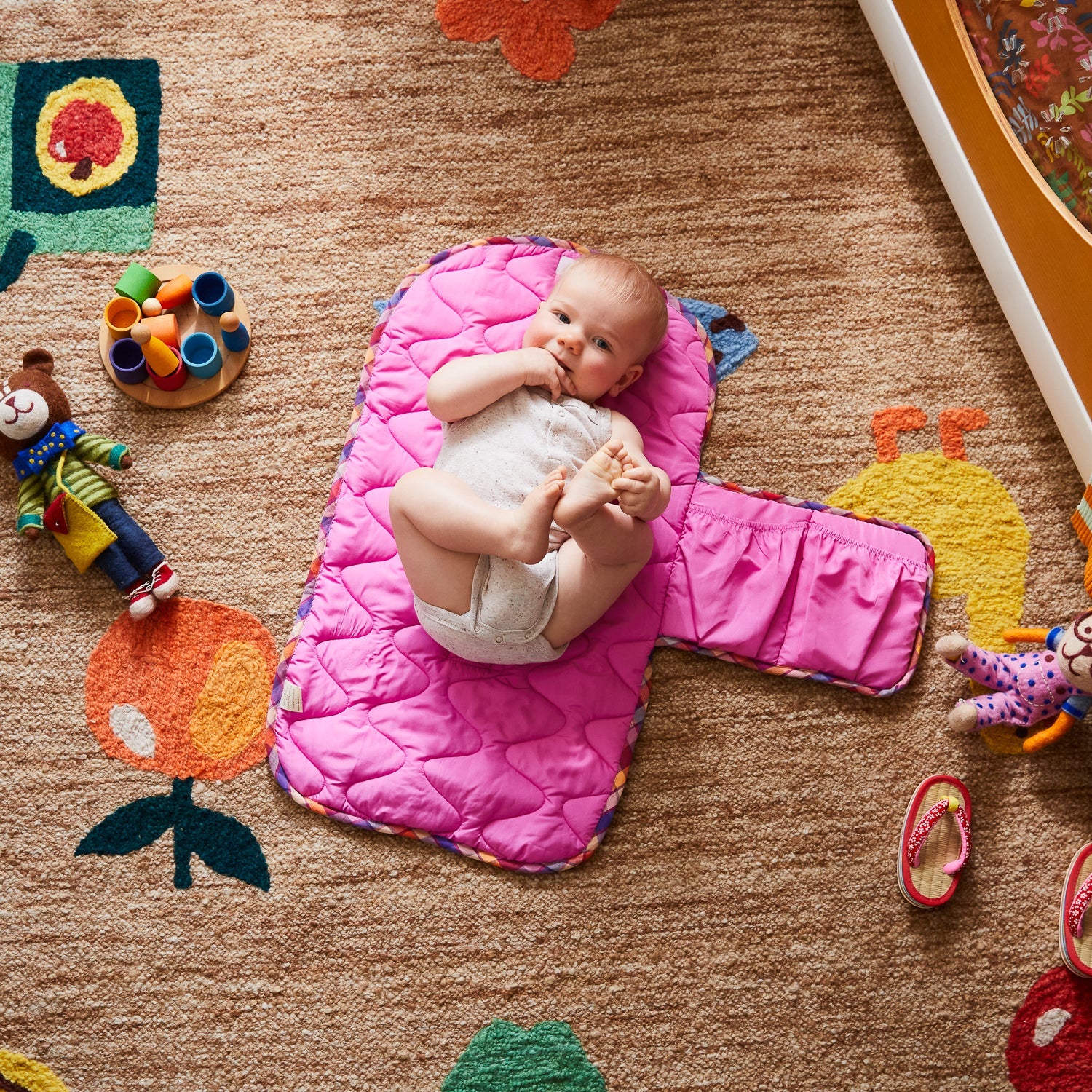 Stela Change Mat in bright pink quilted fabric with baby lying on padded surface surrounded by toys
