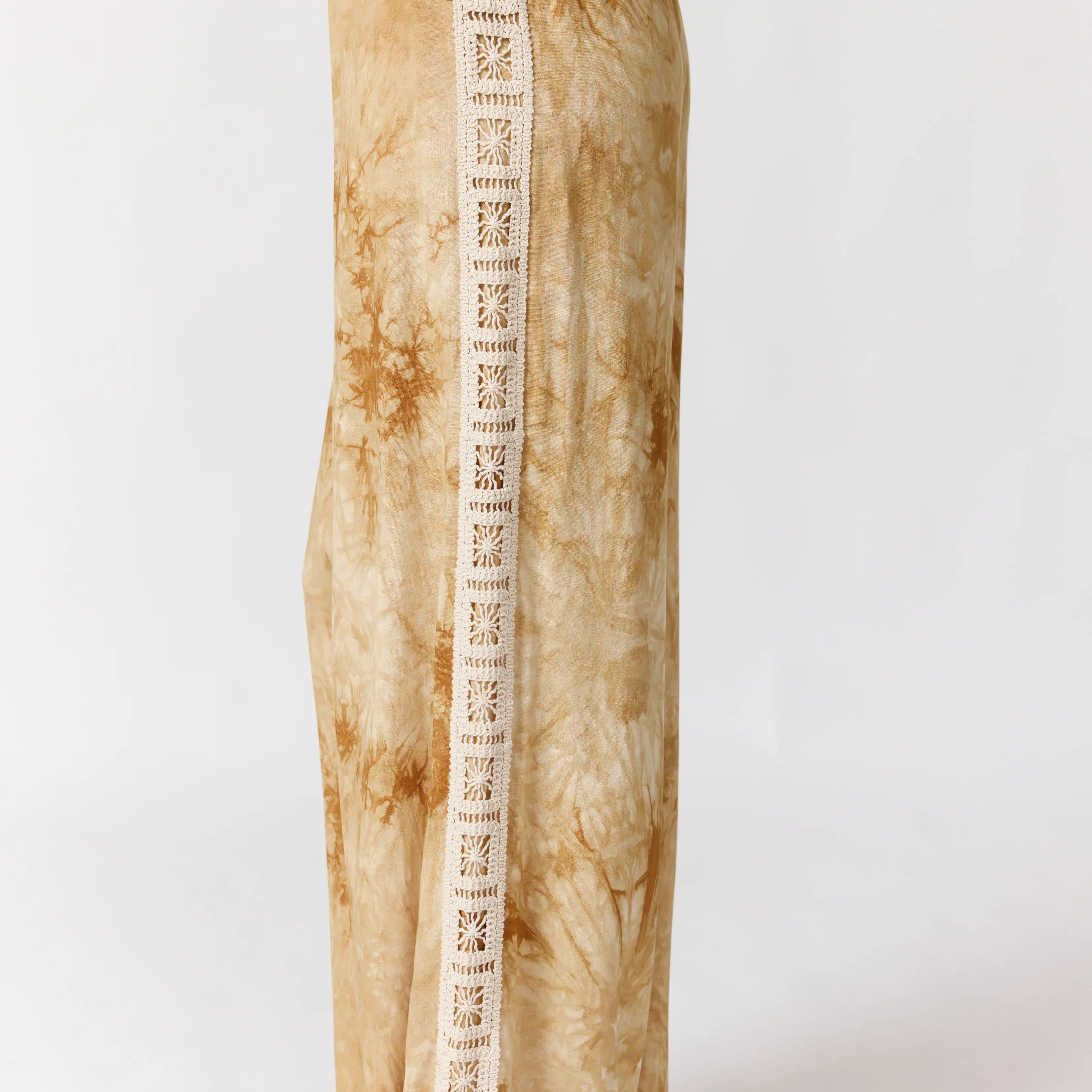 Seated view of Sunday Pants displaying crochet lace trim detail and tie-dye fabric pattern