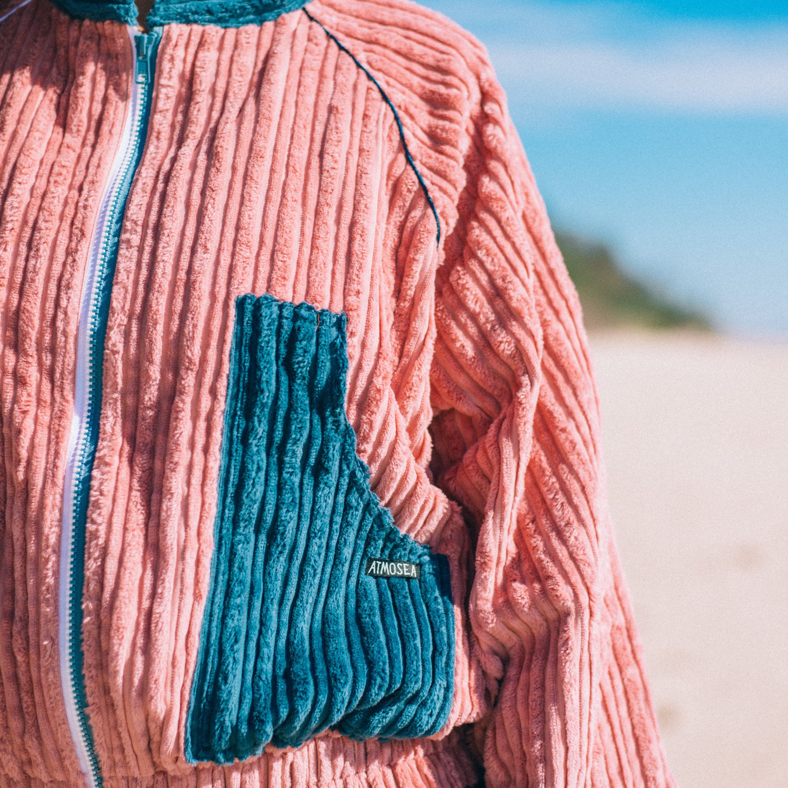 Close-up of pink corduroy surf bomber jacket showing teal contrast chest pocket zip detail and ribbed texture