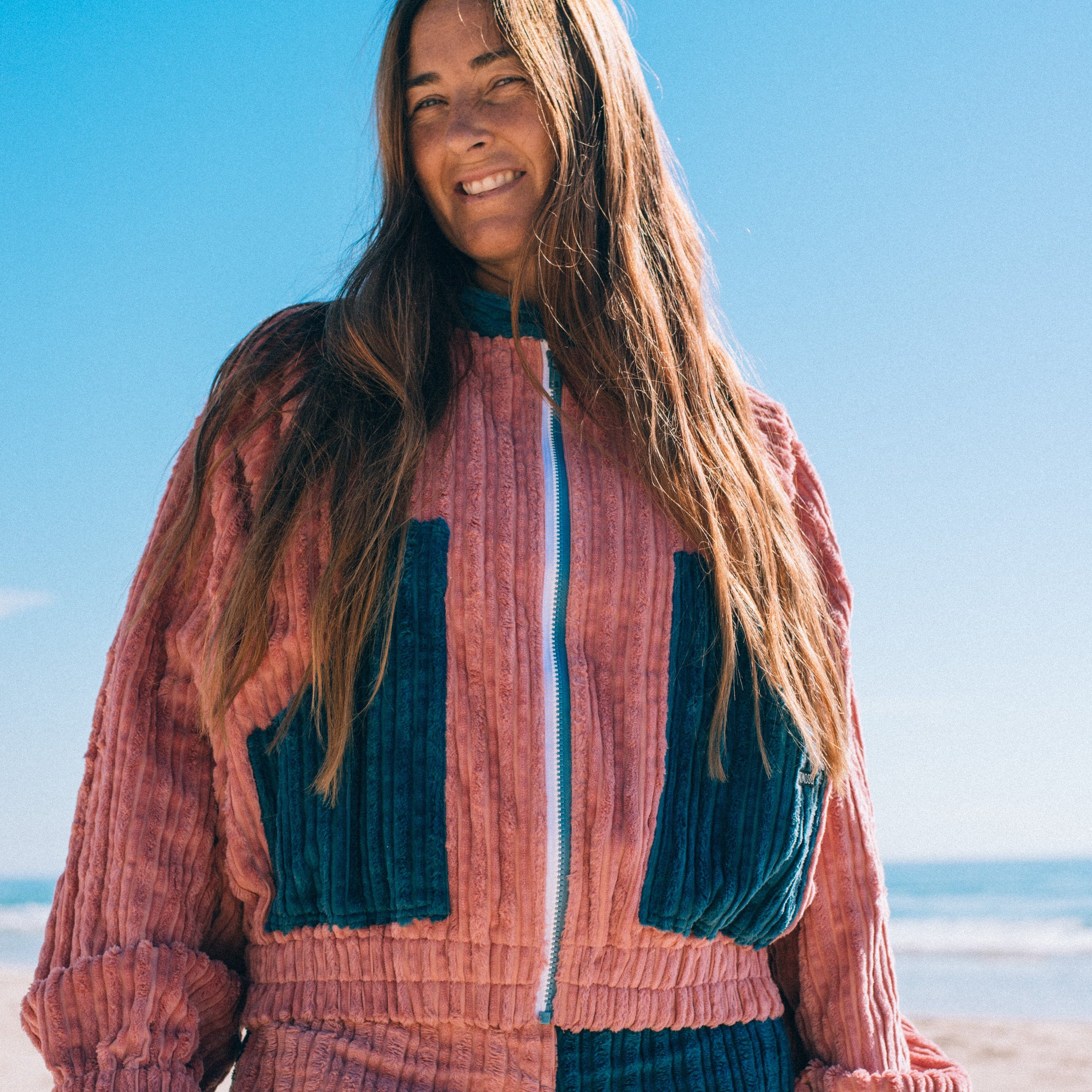 Upper body front view of pink teal two tone corduroy surf bomber jacket showing zip front and elasticated hem