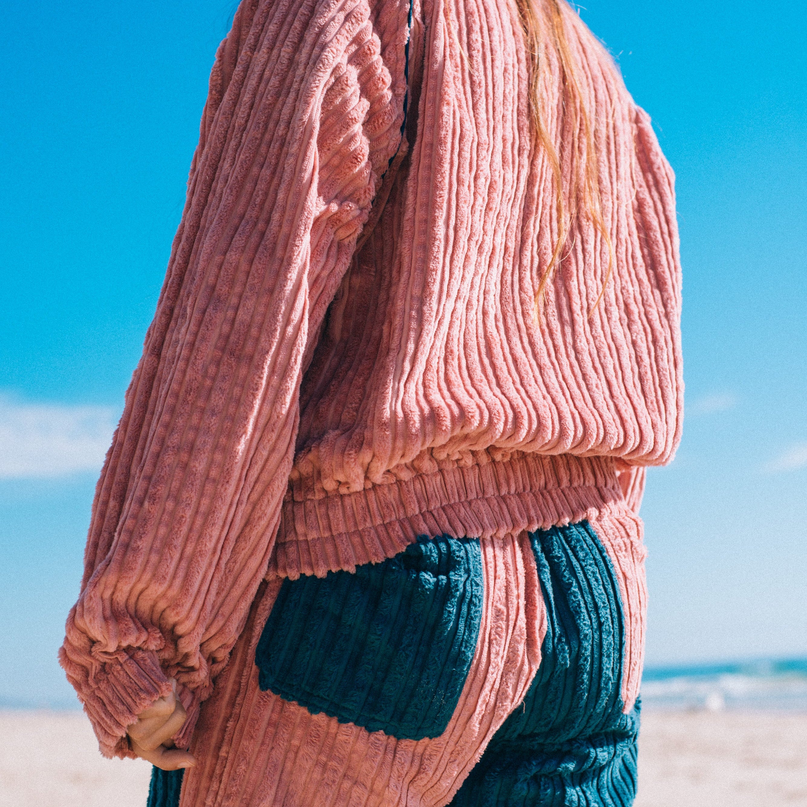 Back view of pink corduroy surf bomber jacket at beach showing ribbed texture elasticated hem and cuffs