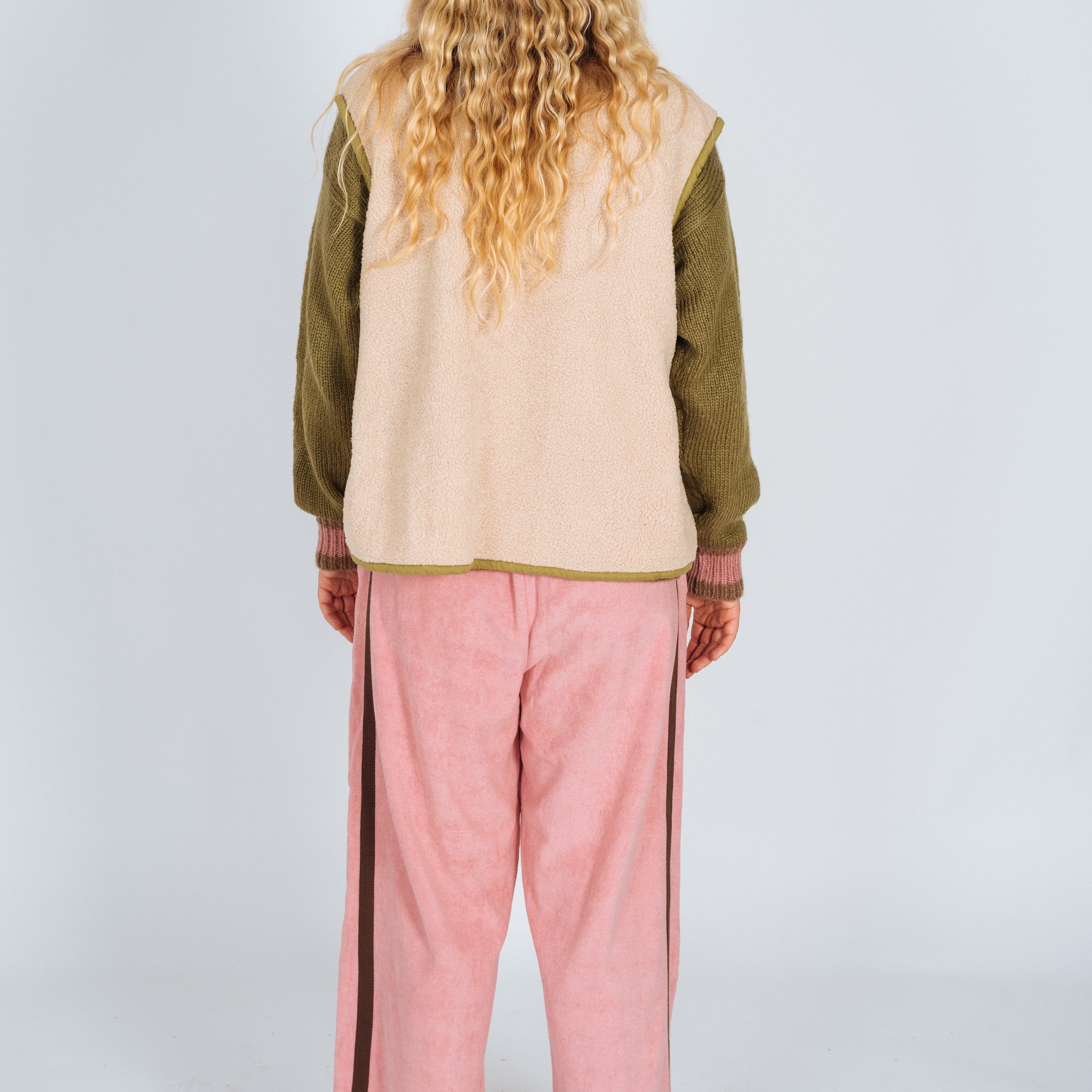 Back view of a cream sherpa front zip vest with olive trim, worn over a knit sweater and pink wide-leg pants