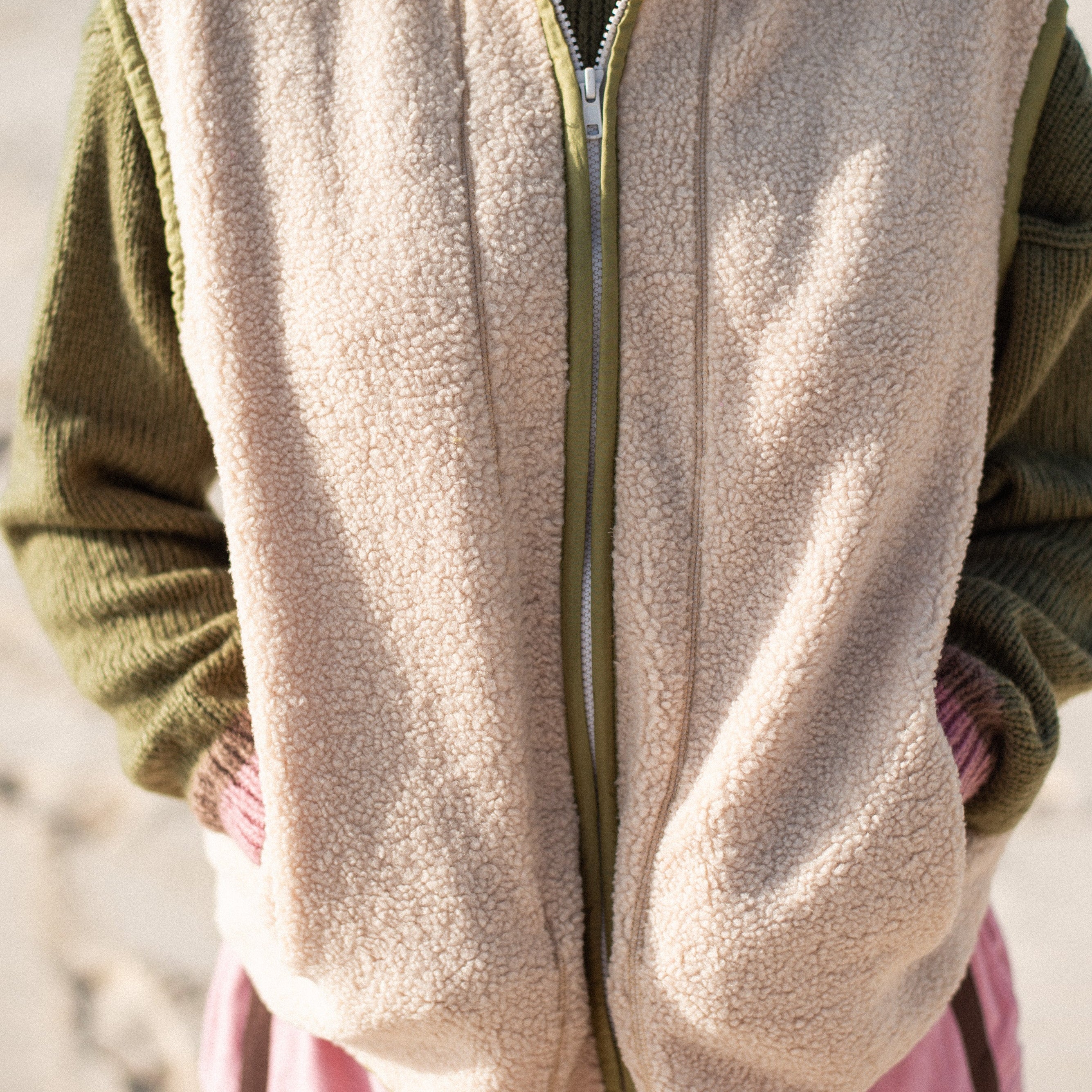 Close-up front detail of a cream sherpa front zip vest showing the zipper and olive trim edging