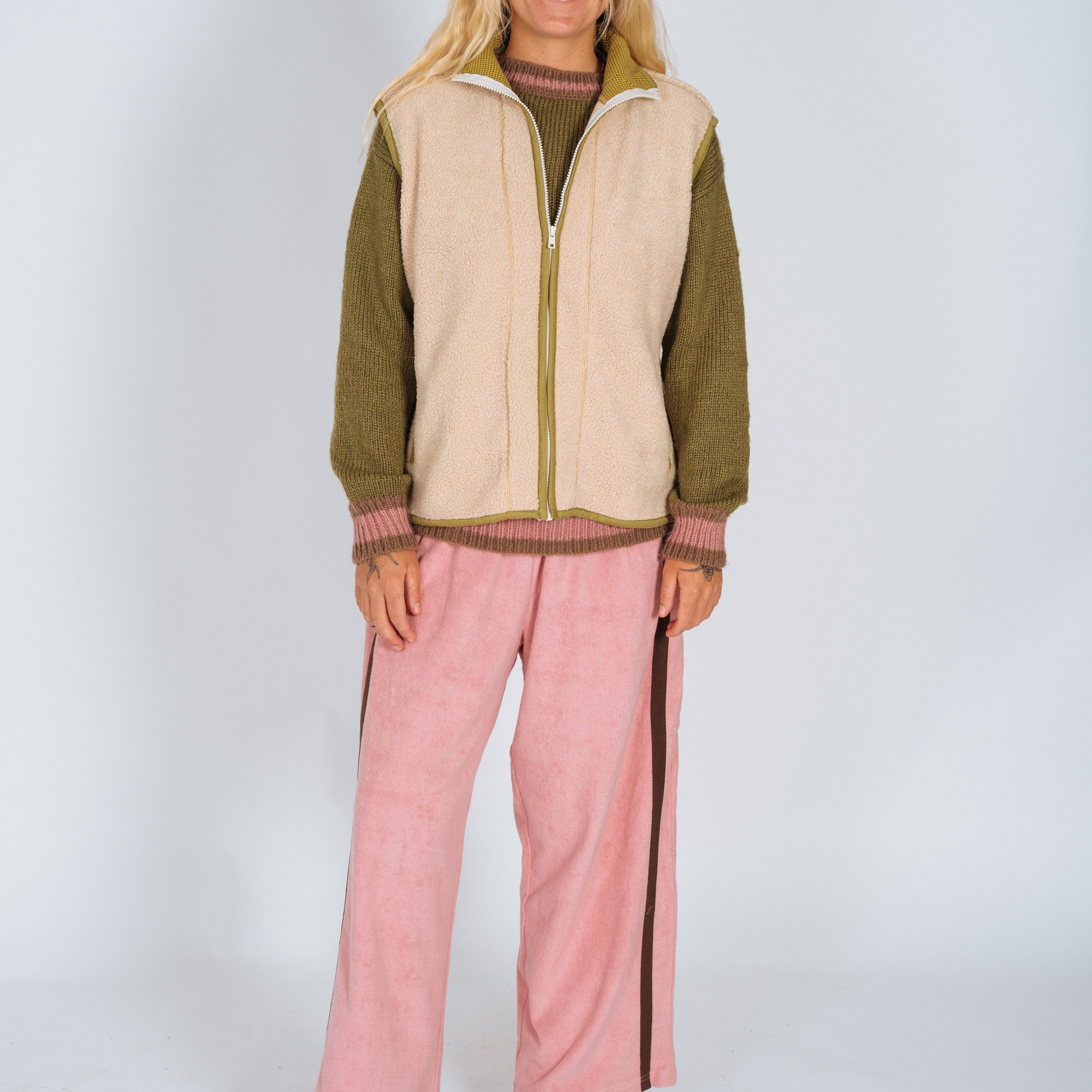 Woman in a cream sherpa front zip vest with olive trim layered over a knit sweater, full-body front view