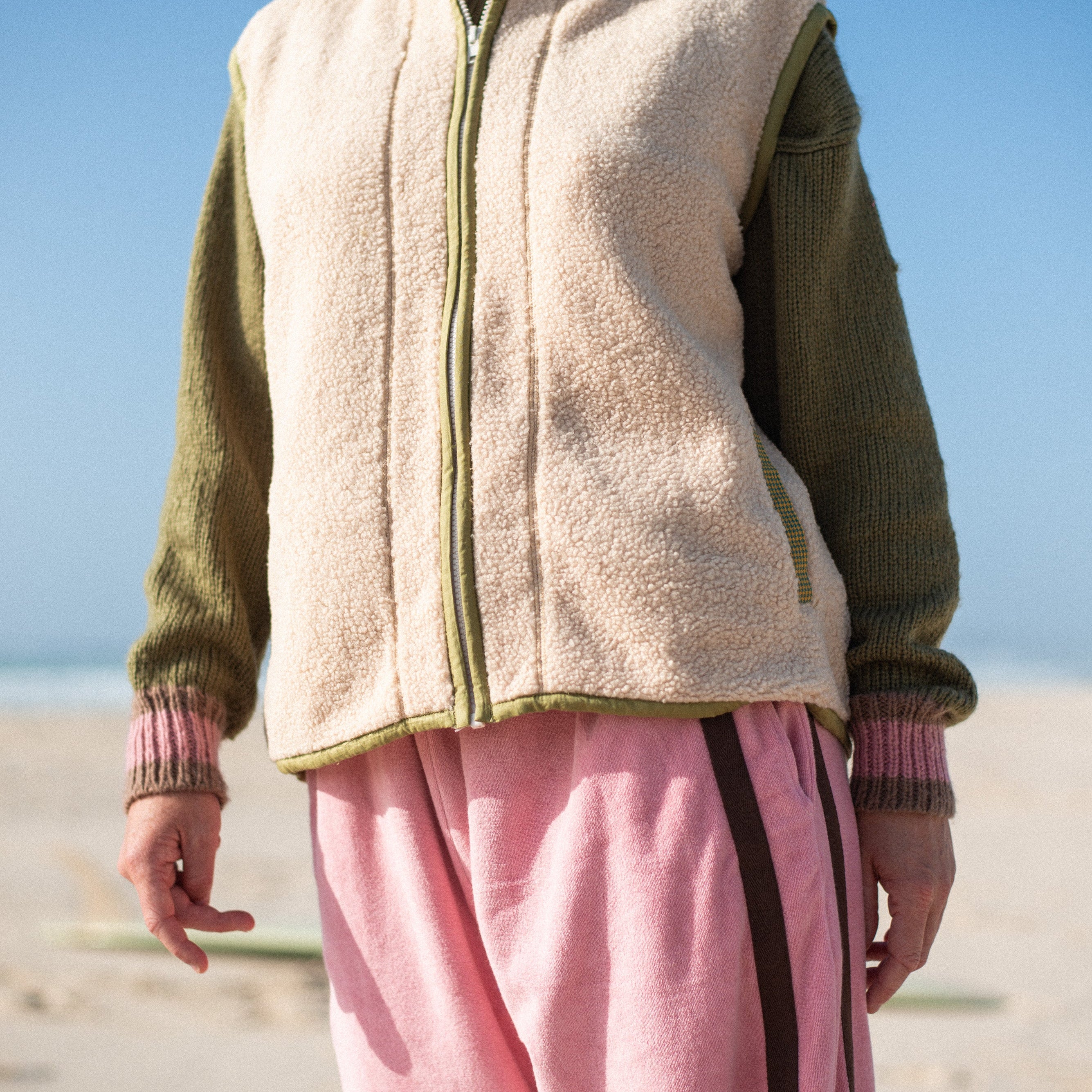 Cream sherpa front zip vest with olive trim worn on the beach, cropped front view in natural light
