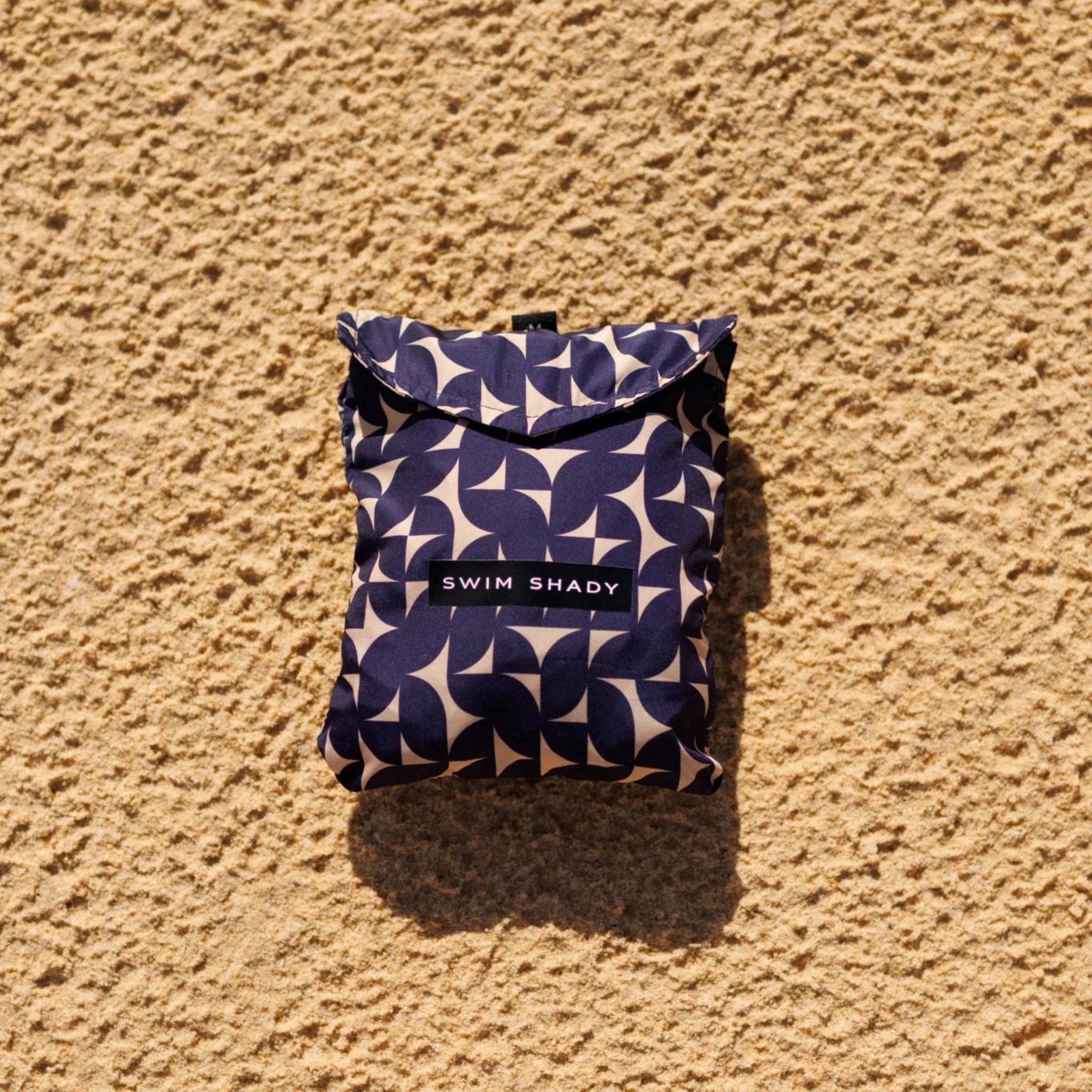 Folded fabric pouch with 'Swim Shady' branding on a beige textured surface