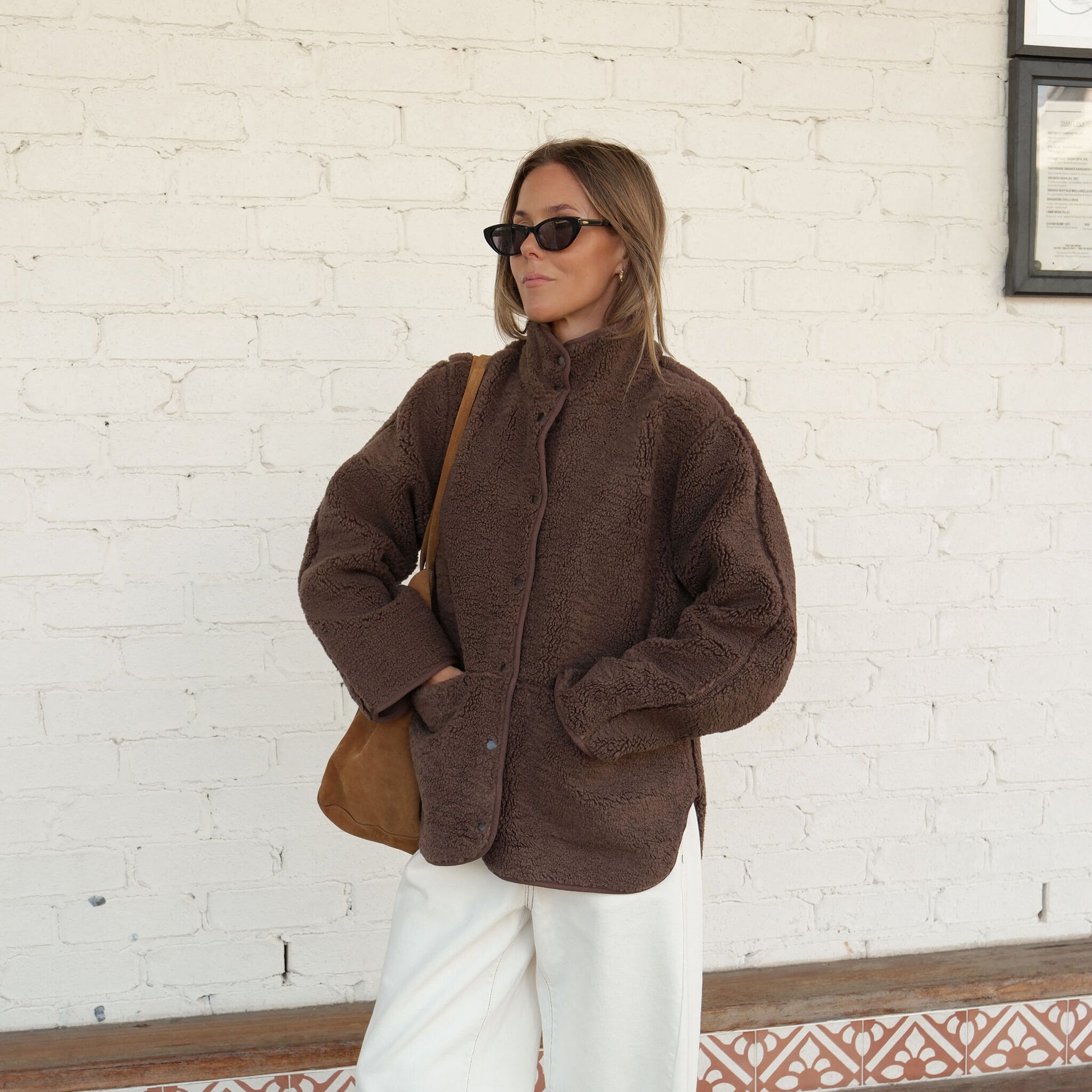 Three quarter view of chocolate brown teddy jacket styled with white pants showing relaxed silhouette