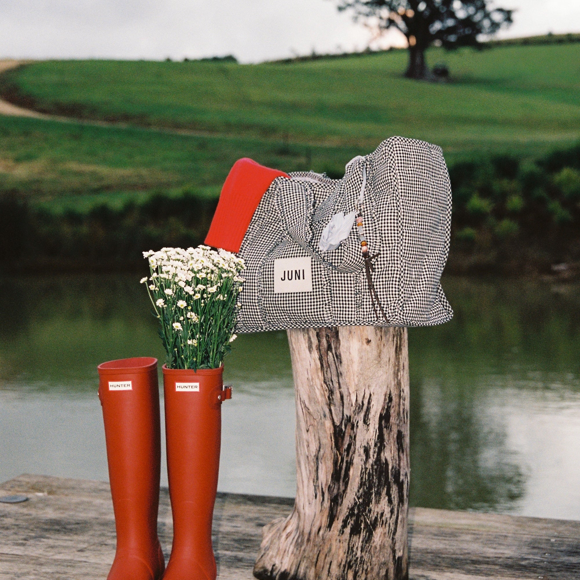 Vichy gingham Everything Bag styled outdoors on wooden post beside red boots and wildflowers