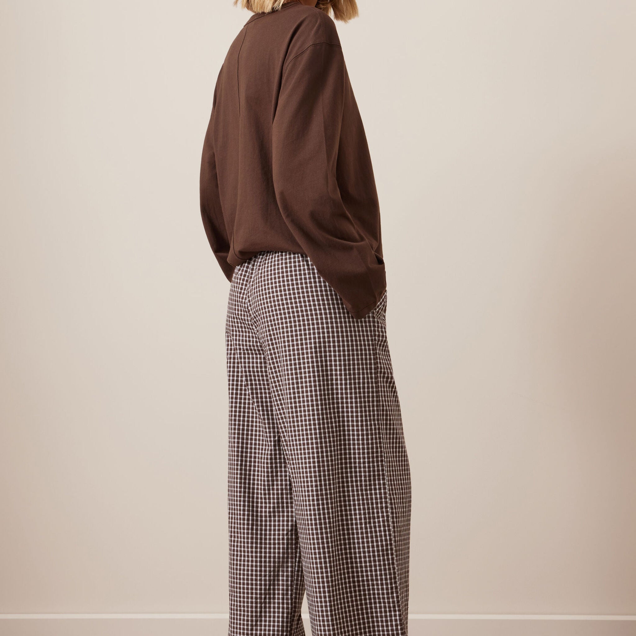 Back three-quarter view of woman in chocolate check lounge pants with brown sweater